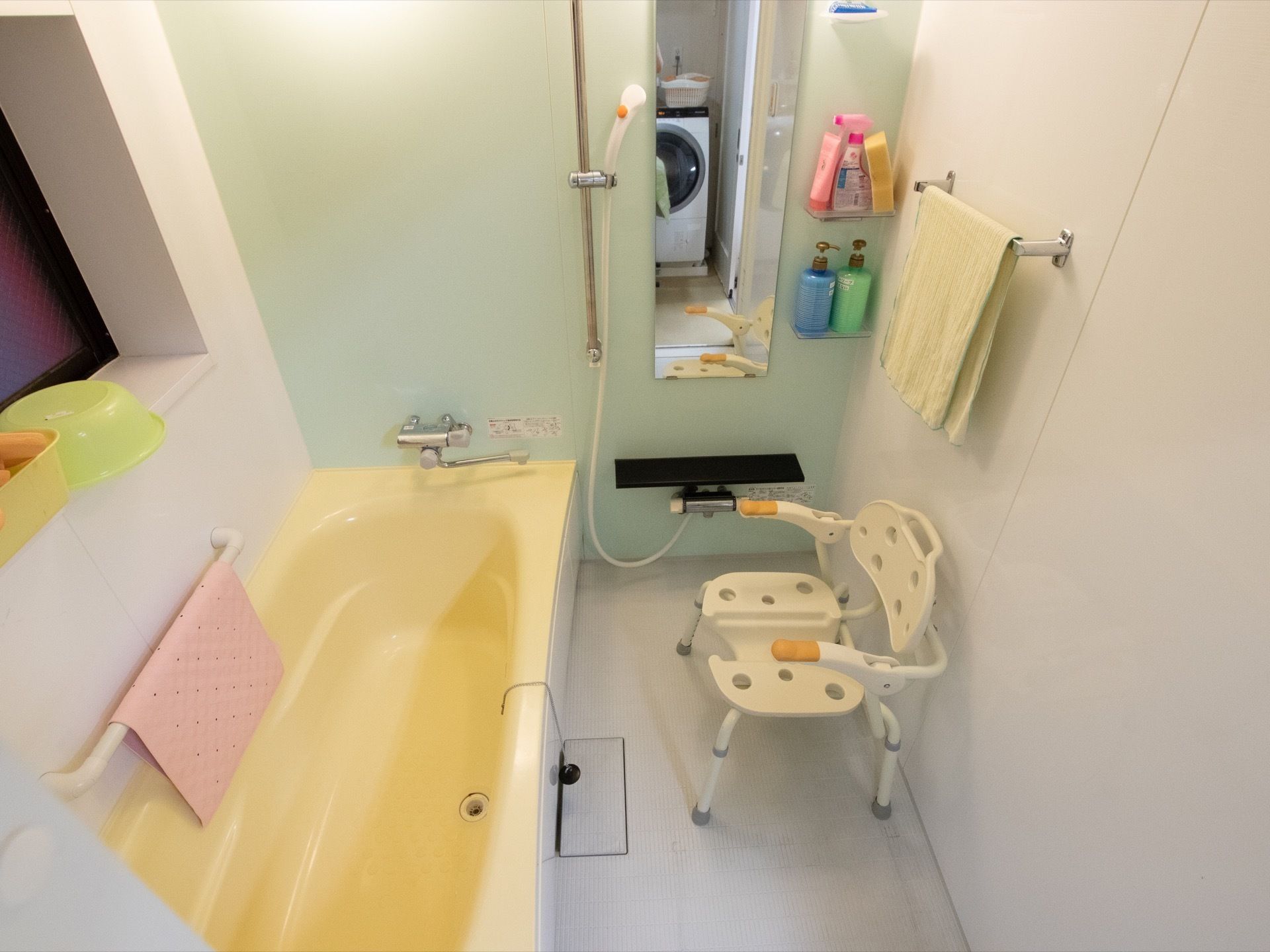 一人用の浴槽がある。黄色いバスタブとミントグリーンの壁面で可愛らしい印象がある。お体を洗う用の背もたれの付いた椅子がある。