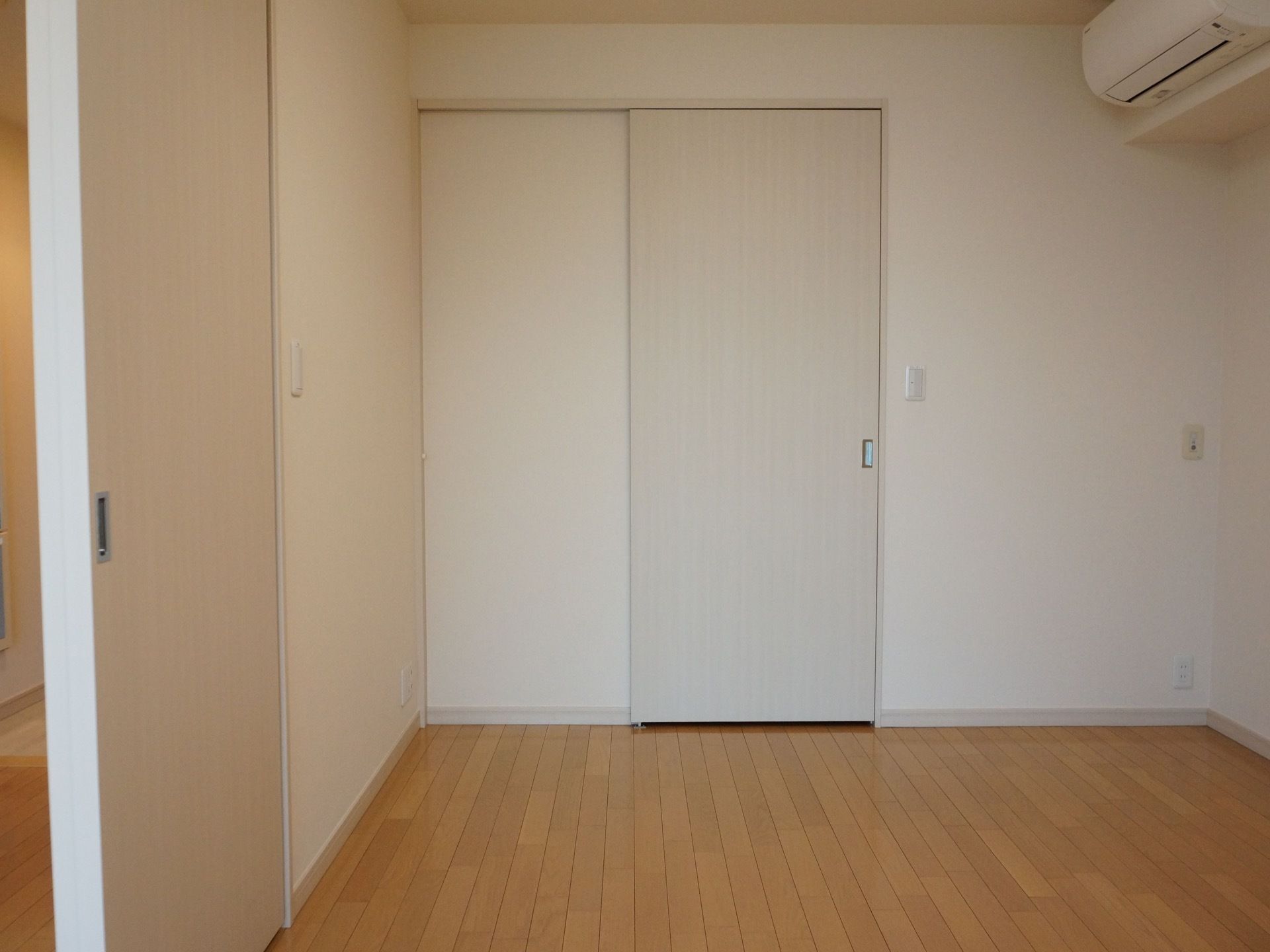 居室は、白い壁とフローリングの床で統一されたシンプルな内装となっている。部屋の敷居には、白い引戸が取りつけられている。