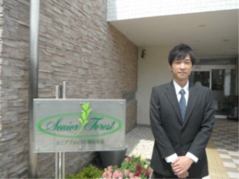 スーツを着た施設の男性職員が、入り口前に立っている様子