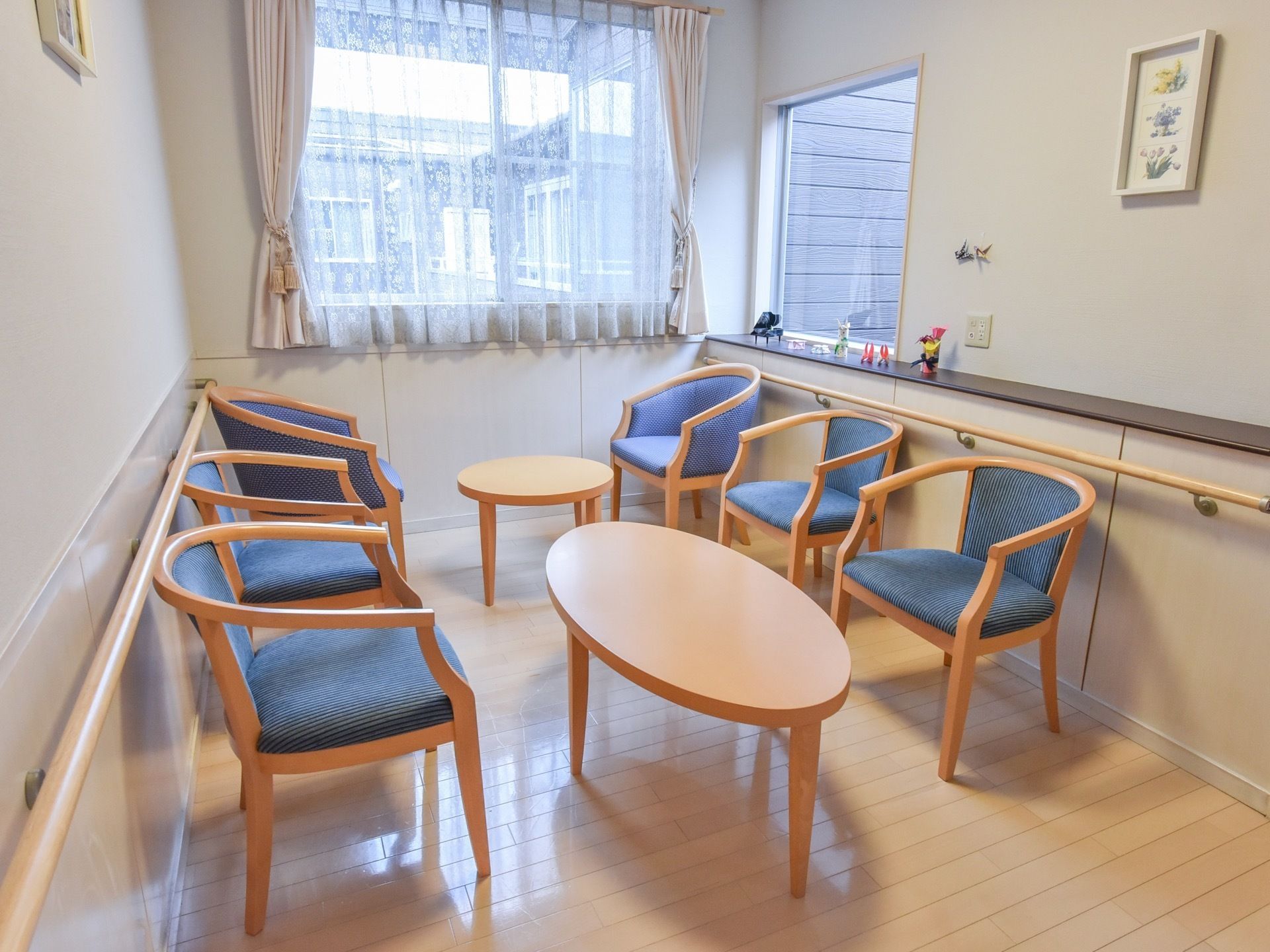 窓が大きく明るく清潔な部屋である。テーブルが２卓、椅子が６脚置いてある。壁には小さな絵が掛けられ、棚には小さな小物類が飾られている。