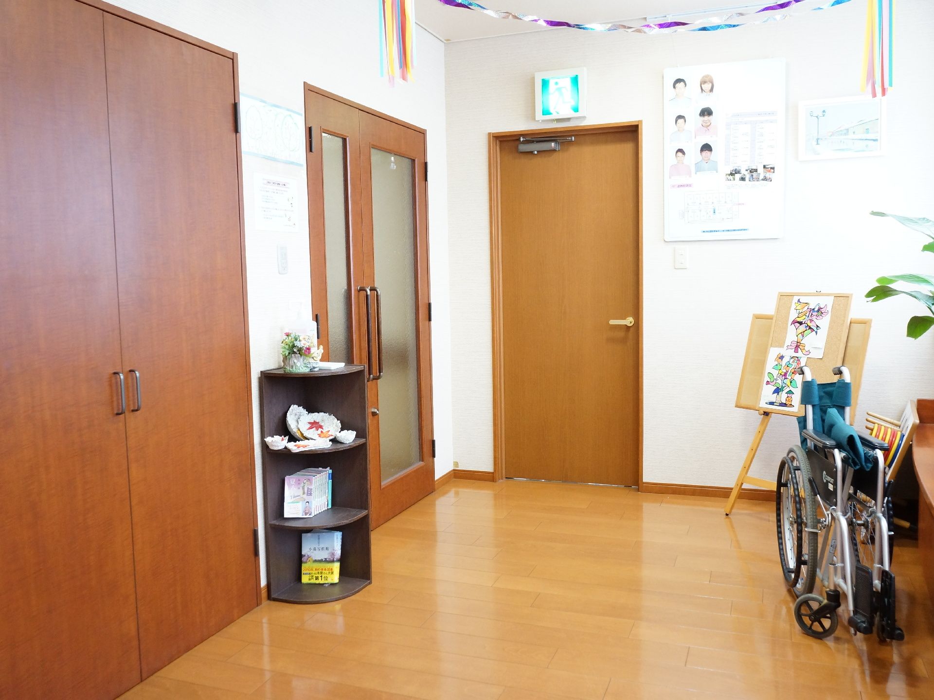 白色の壁と木目の床の内装の通路スペースである。横側には窓があり、その下には台が設けられ観葉植物が飾ってある。
