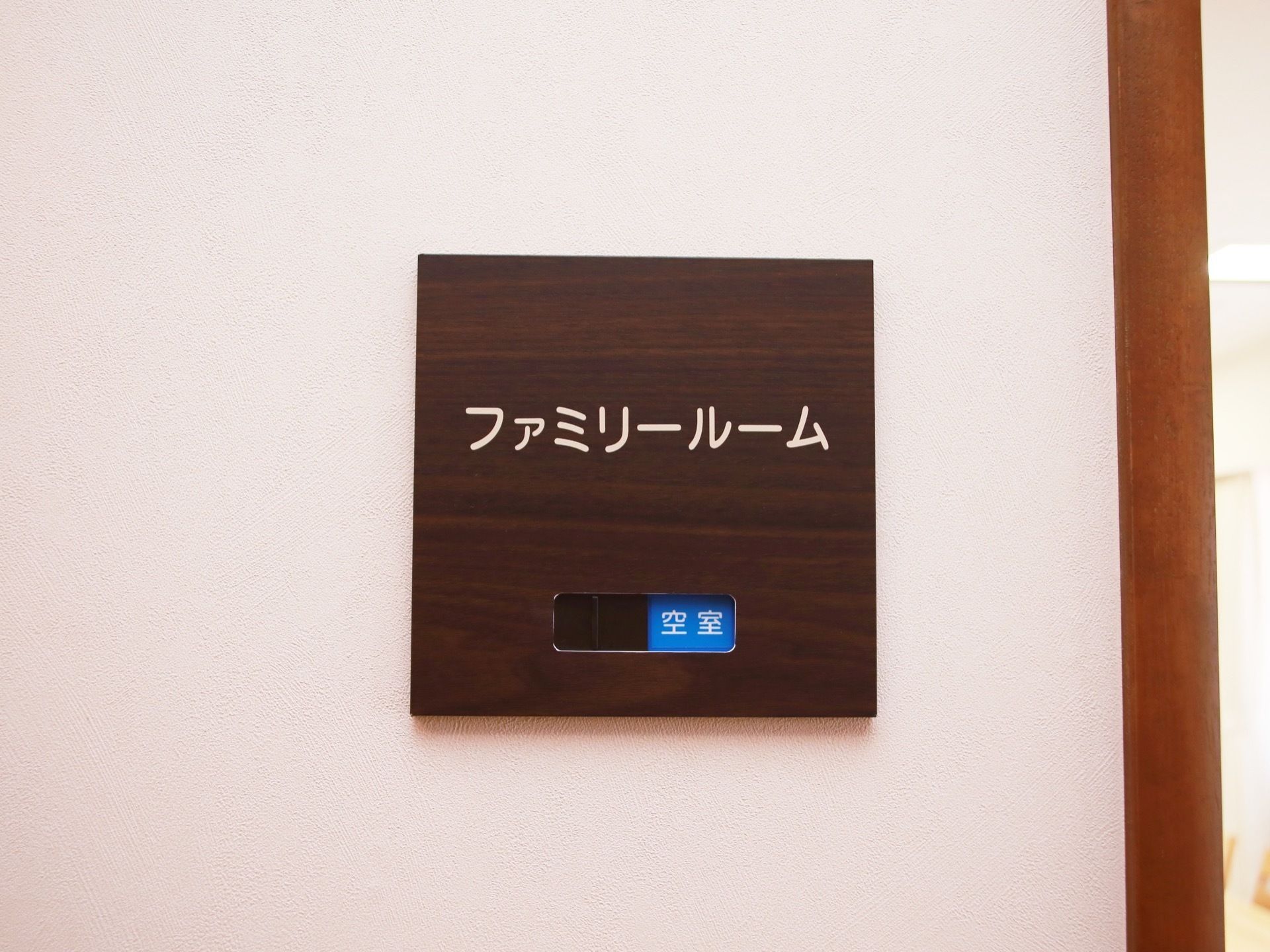 暗い木目調の四角い看板に、ファミリールームと白抜きで表示されている。下部に、空室であることを知らせる青い表示がある。