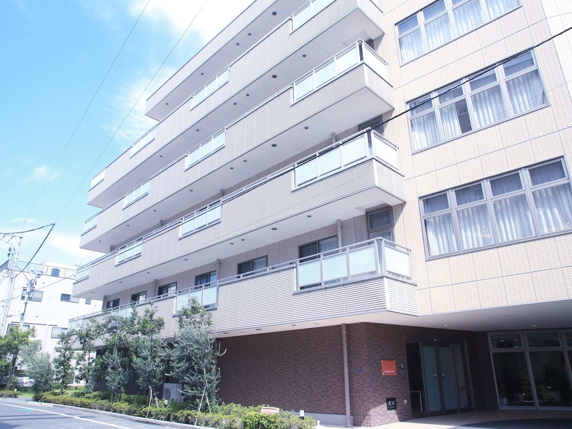道路沿いに植栽が施され、その内側に鉄骨造りの施設がある。地上５階建ての窓が多く設置された建物である。