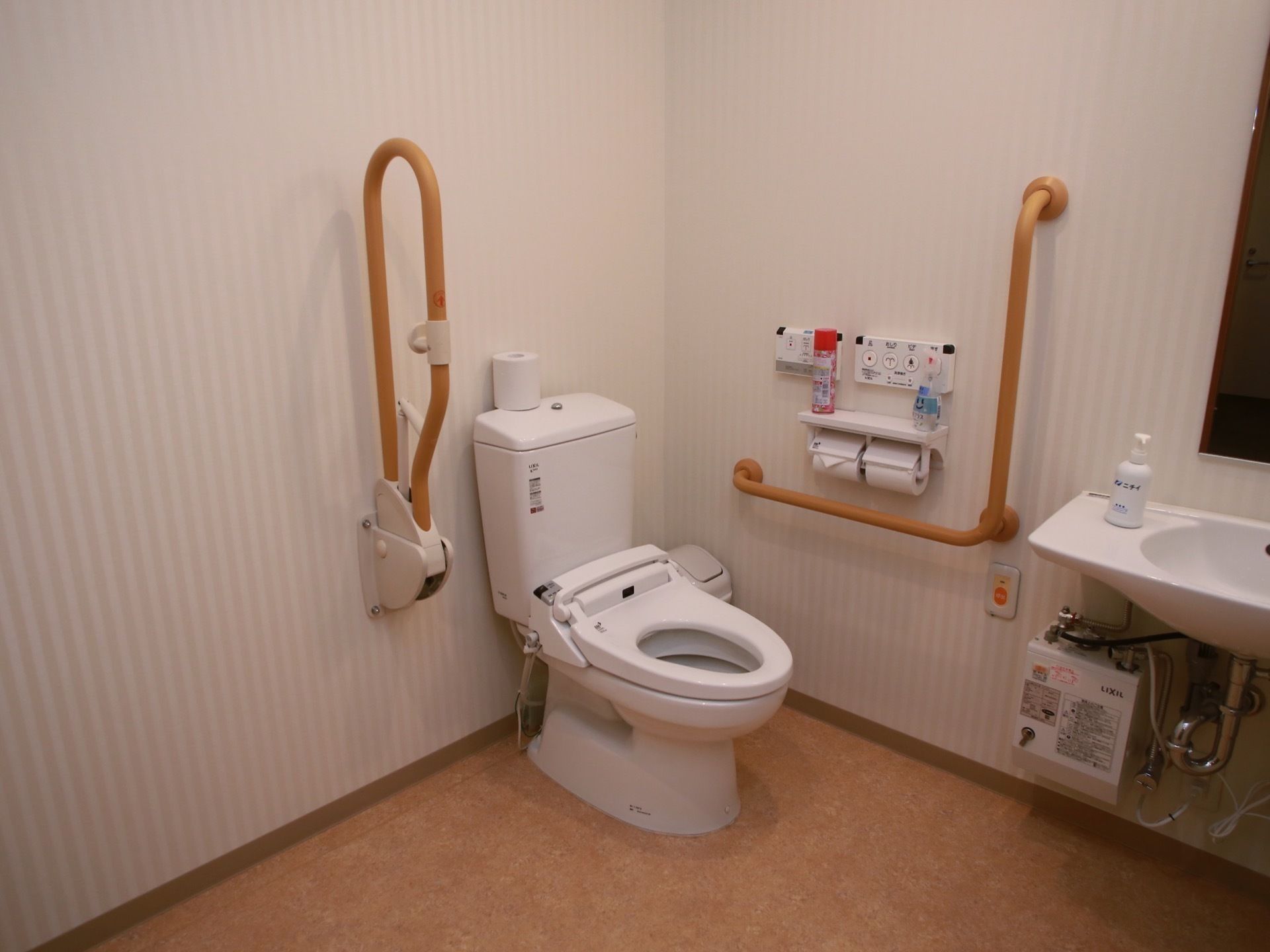 広々としたトイレ空間に、蓋のない洋式便器が据えられている。手前のグリップは上げ下ろしができるので、便器に座るときに邪魔にならない。