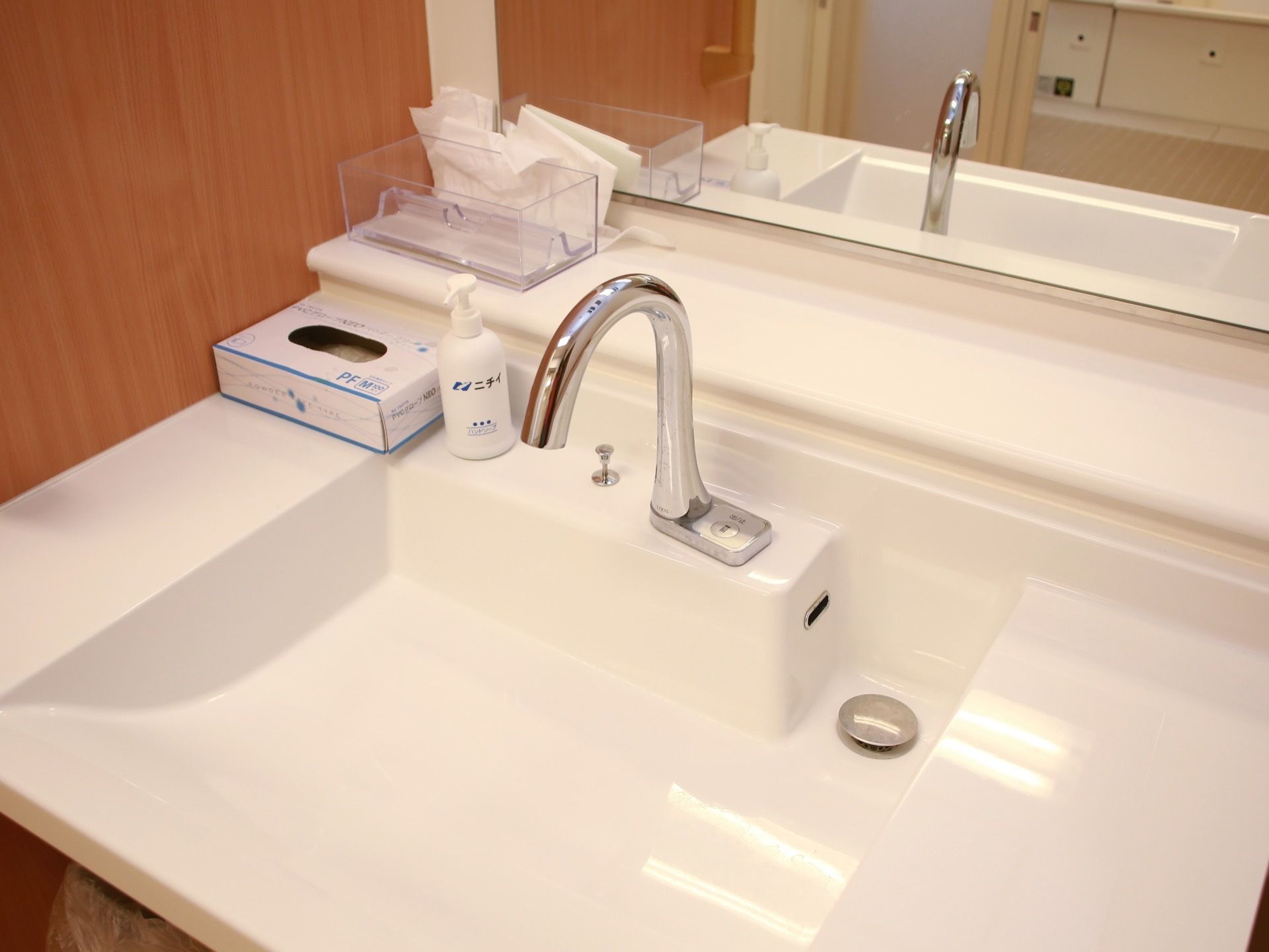 幅が広い角形のスタイリッシュな洗面台が鏡の前に設置されている。自動水栓の隣にポンプ式ボトルが置かれている。