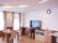明るい広間の壁面に時計が掛かっており、その下の棚に大型液晶テレビが置かれている。右側に洗面台が見える。