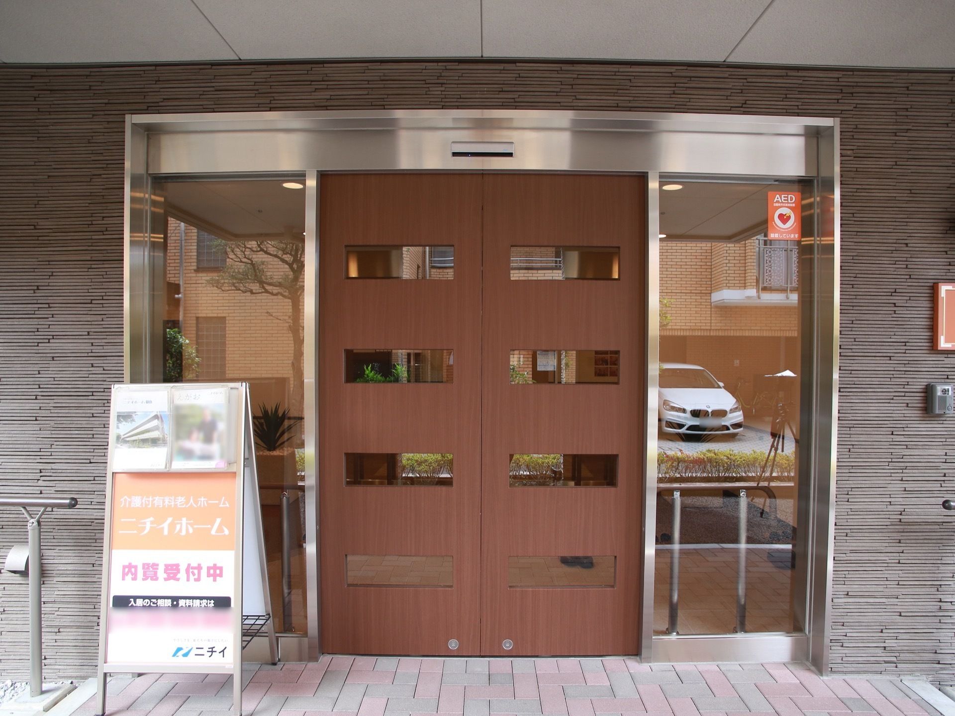 玄関の扉は木製の両開きの自動ドアである。扉には小窓が４つずつあり、少しだけ中の様子が見える。ドアの手前には立て看板がある。