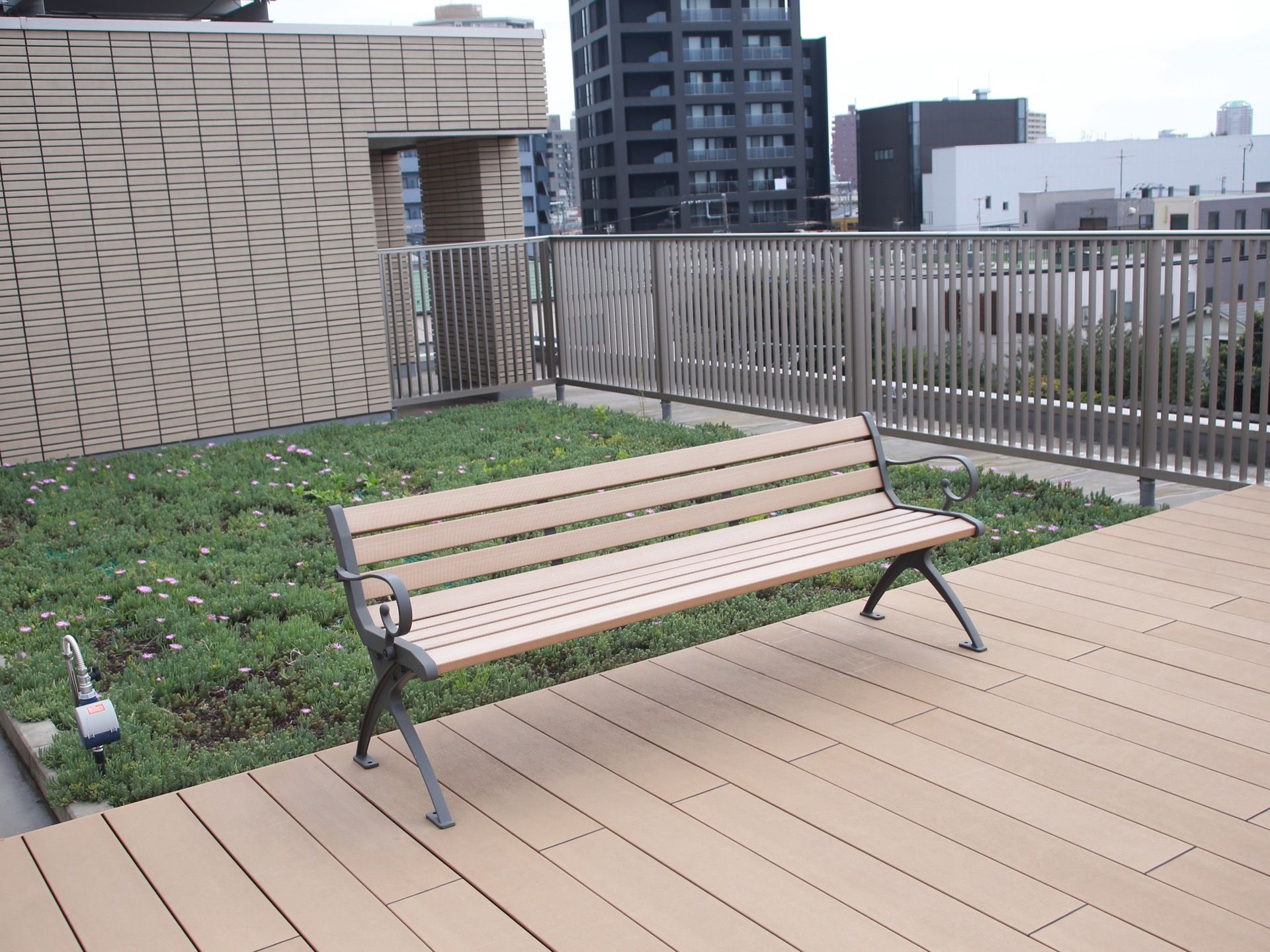 ルーフデッキに設置されたベンチの後ろにある正方形の花壇は、屋上庭園である。芝生のような緑の中に、可愛らしい花々が咲いている。