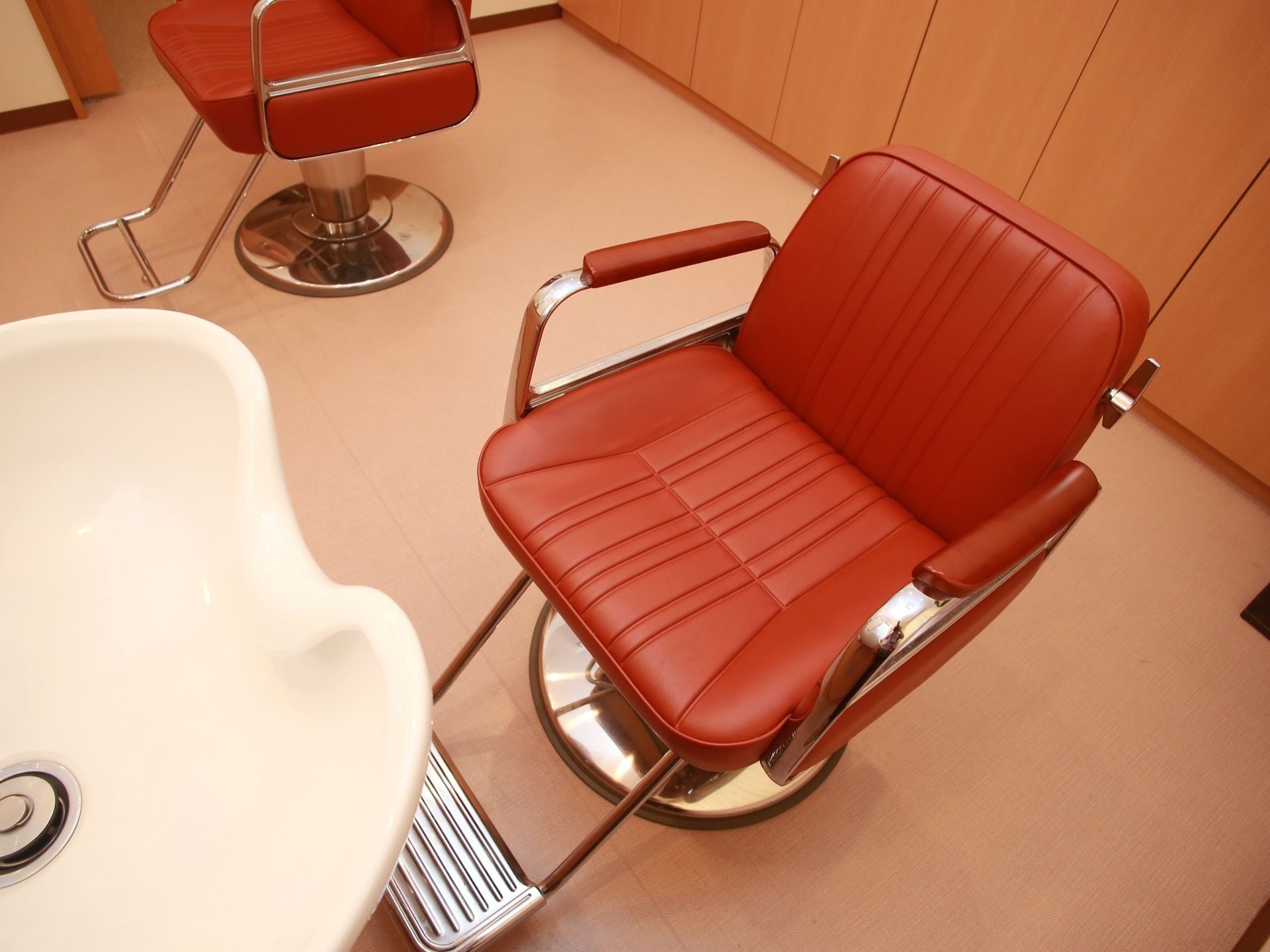 ヘアーサロンはあたたかみのある色調の部屋で、赤いレザー張りのスタイリングチェアが２脚用意されている。散髪や洗髪などのサービスを受けられる。