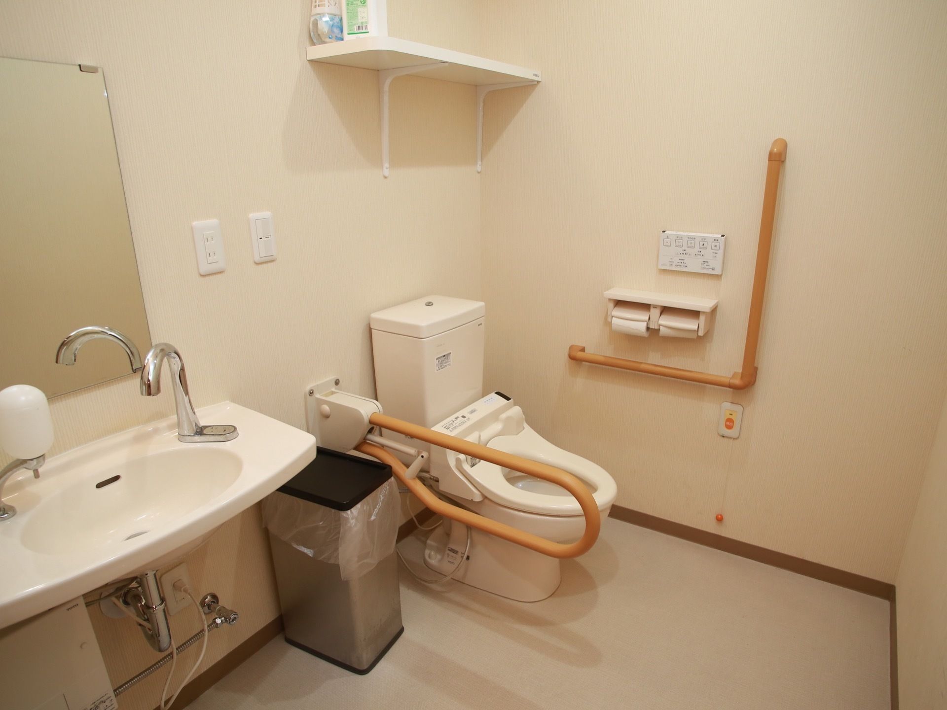 横幅が広い空間に、蓋がない洋式便器、ステンレス製のゴミ箱、鏡と手洗器が設置されている。便器の周囲に手すりが施されており、動きやすい。