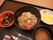 肉と野菜の丼物、味噌汁、五目煮、たくあん漬けが配膳されている。箸と共に、小さめのスプーンとフォークが並べられている。