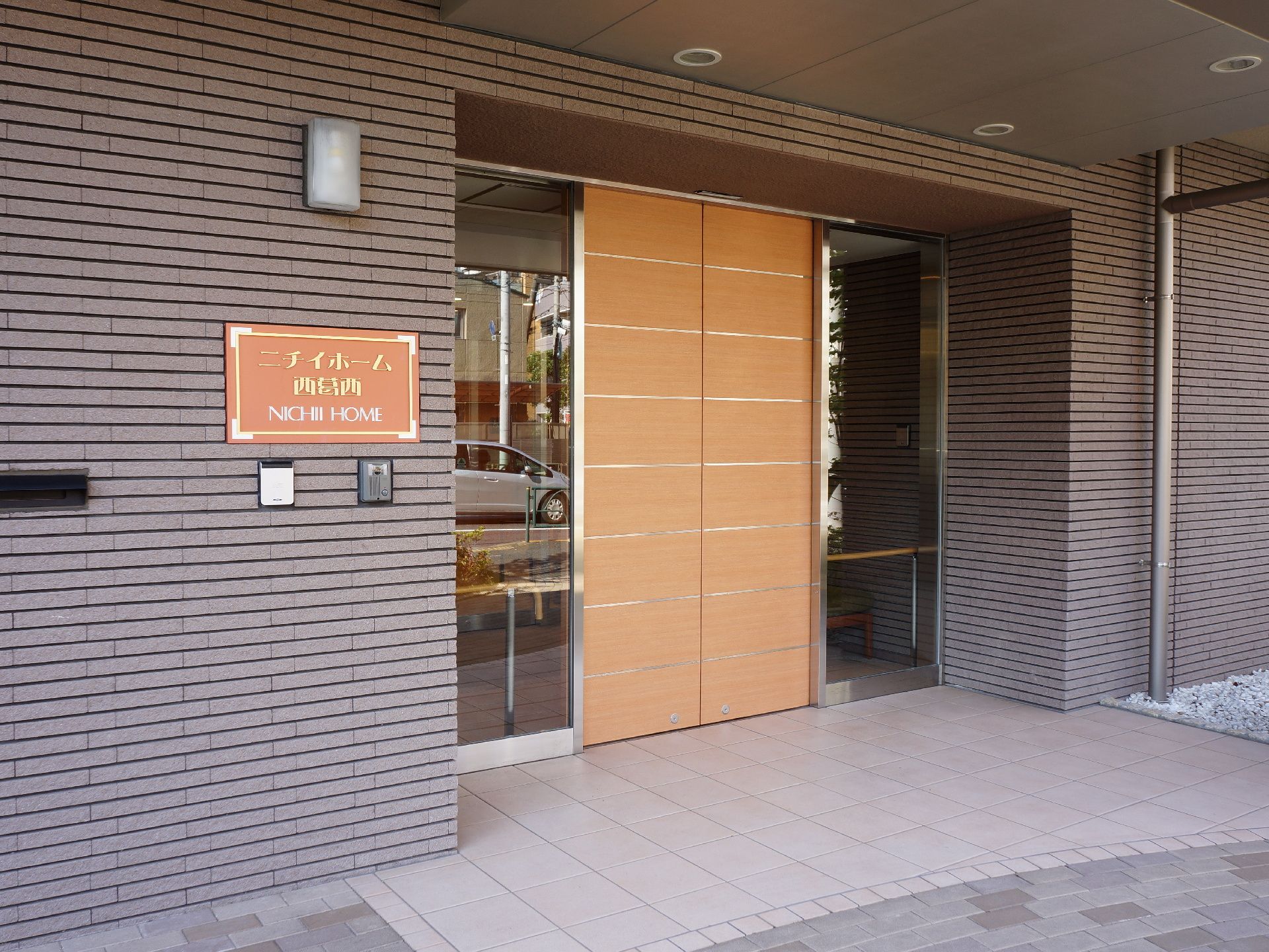 施設の玄関は、落ち着いた色合いのレンガ造り風である。自動ドアの扉は木製で、両側にガラスが付いている。