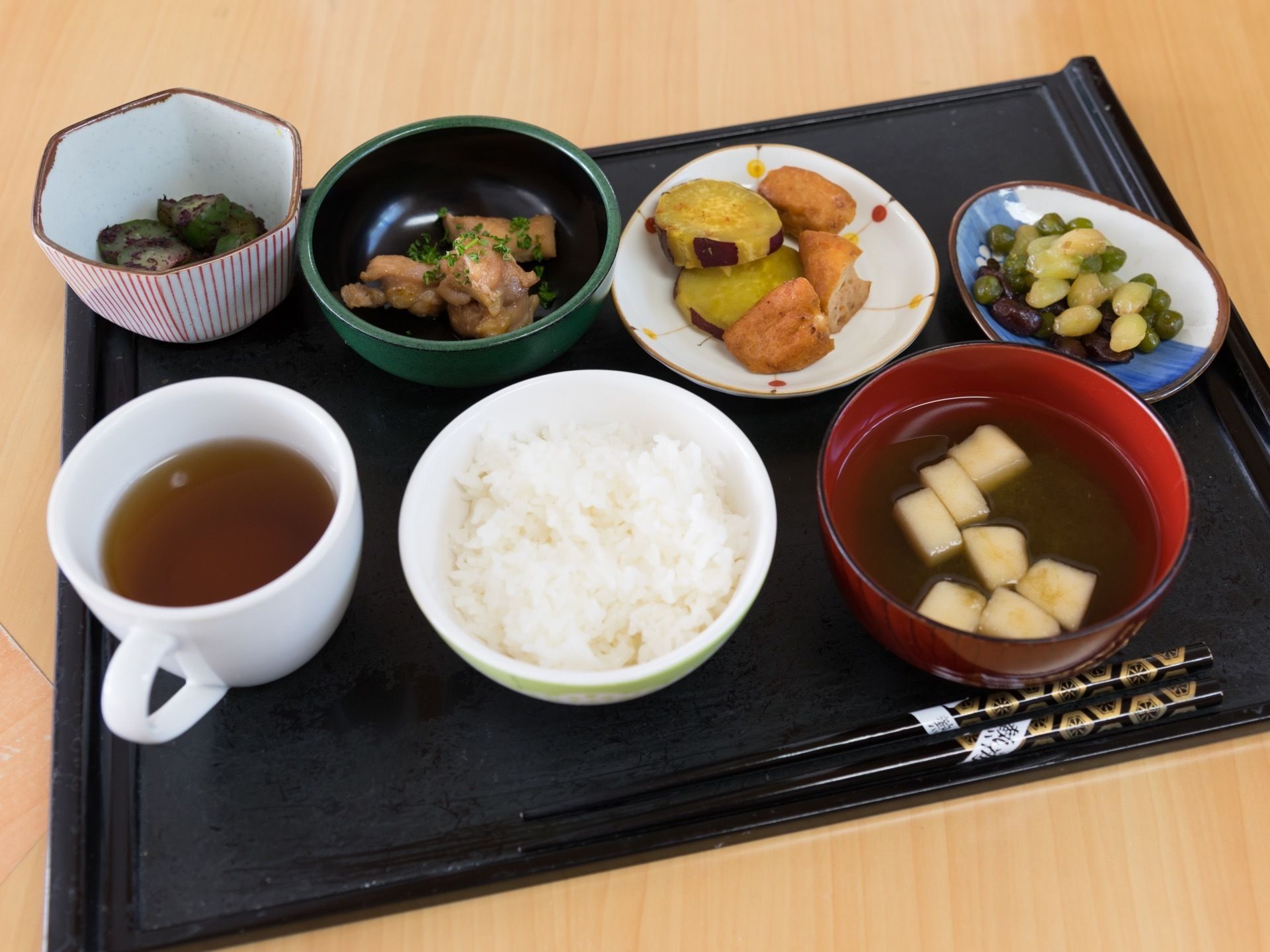 黒色のトレーの上に、ご飯とお吸い物、おかずを４品セットした品数が豊富な食事である。また、コーヒーカップにお茶を入れて添えている。