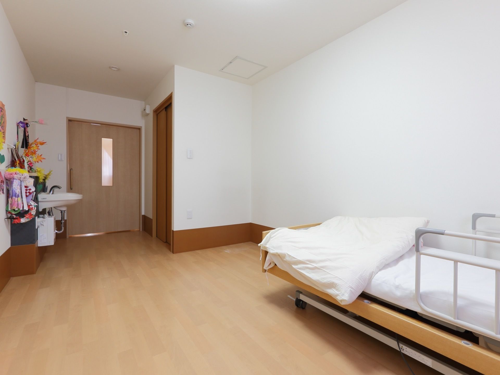 白壁のシンプルな内装の居室には、介護ベッドと洗面台が備え付けられている。入口すぐのトイレは引き戸になっている。
