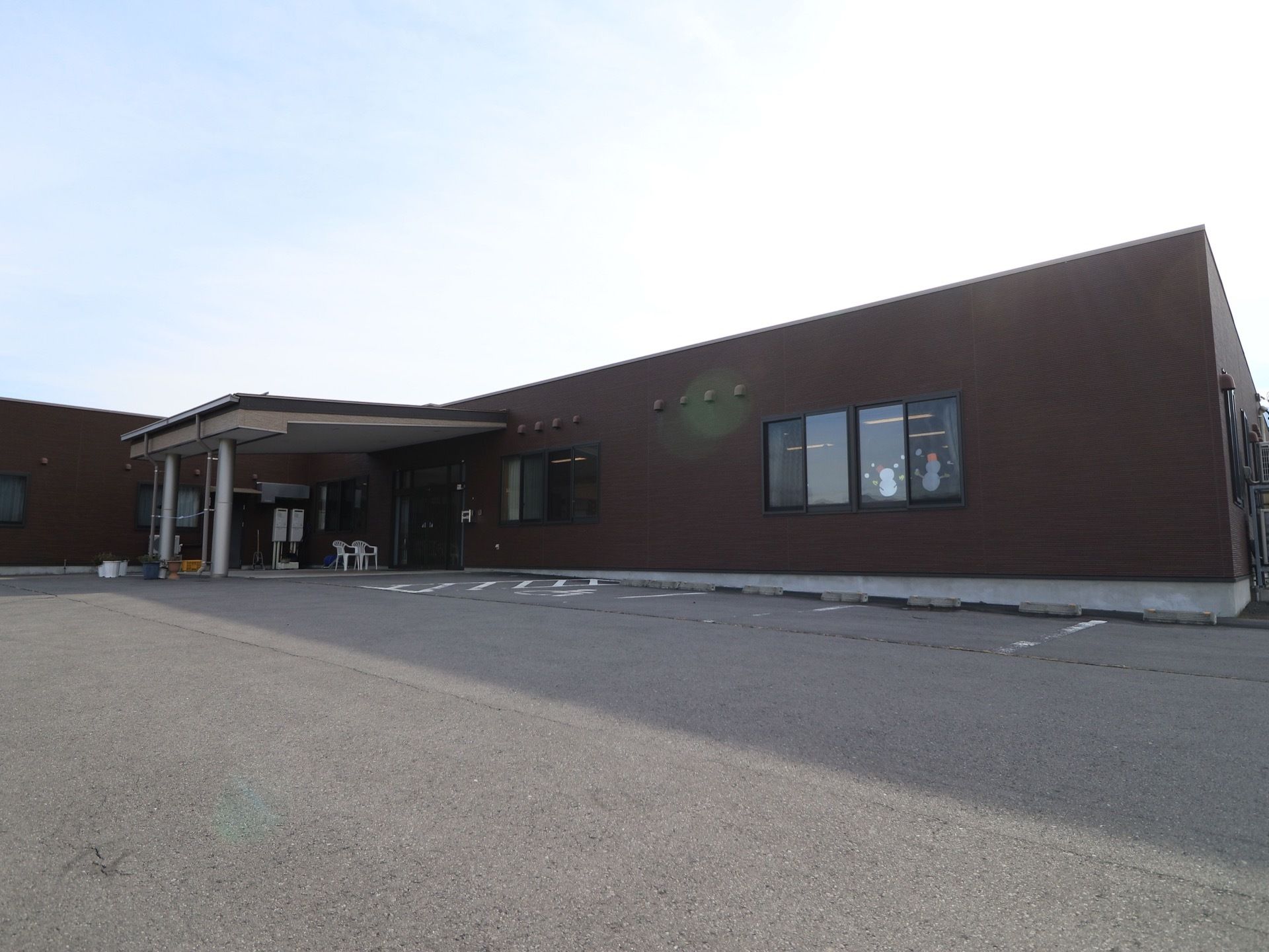 平屋の建物で、玄関の上には屋根が設置されている。建物に沿って車を停めることができ、玄関側は車椅子マークがついている。