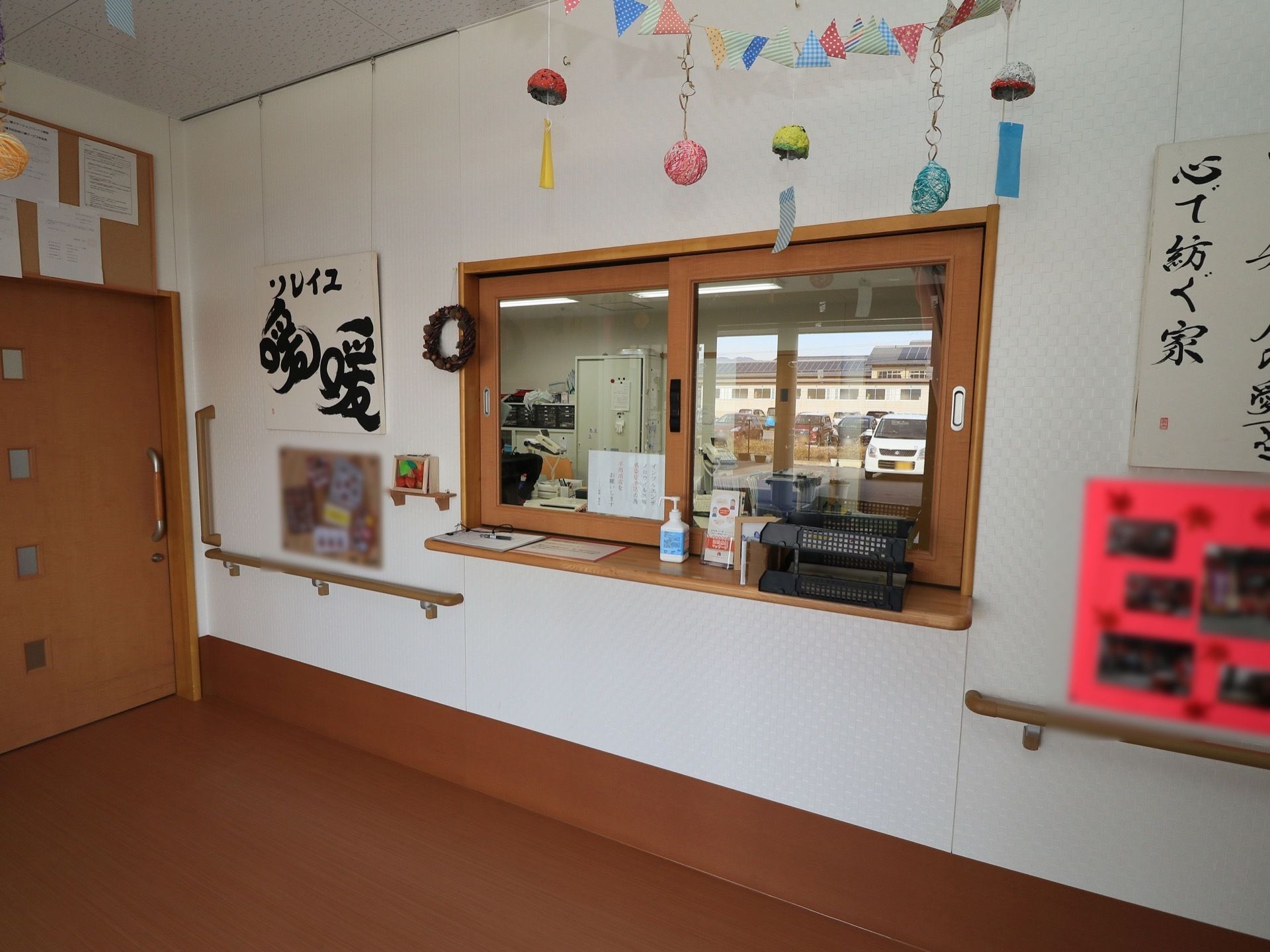 受付のカウンターの周りには、施設名が書かれた看板の他にもコルクボードに写真が飾ってある。カウンターの上には、消毒液がある。