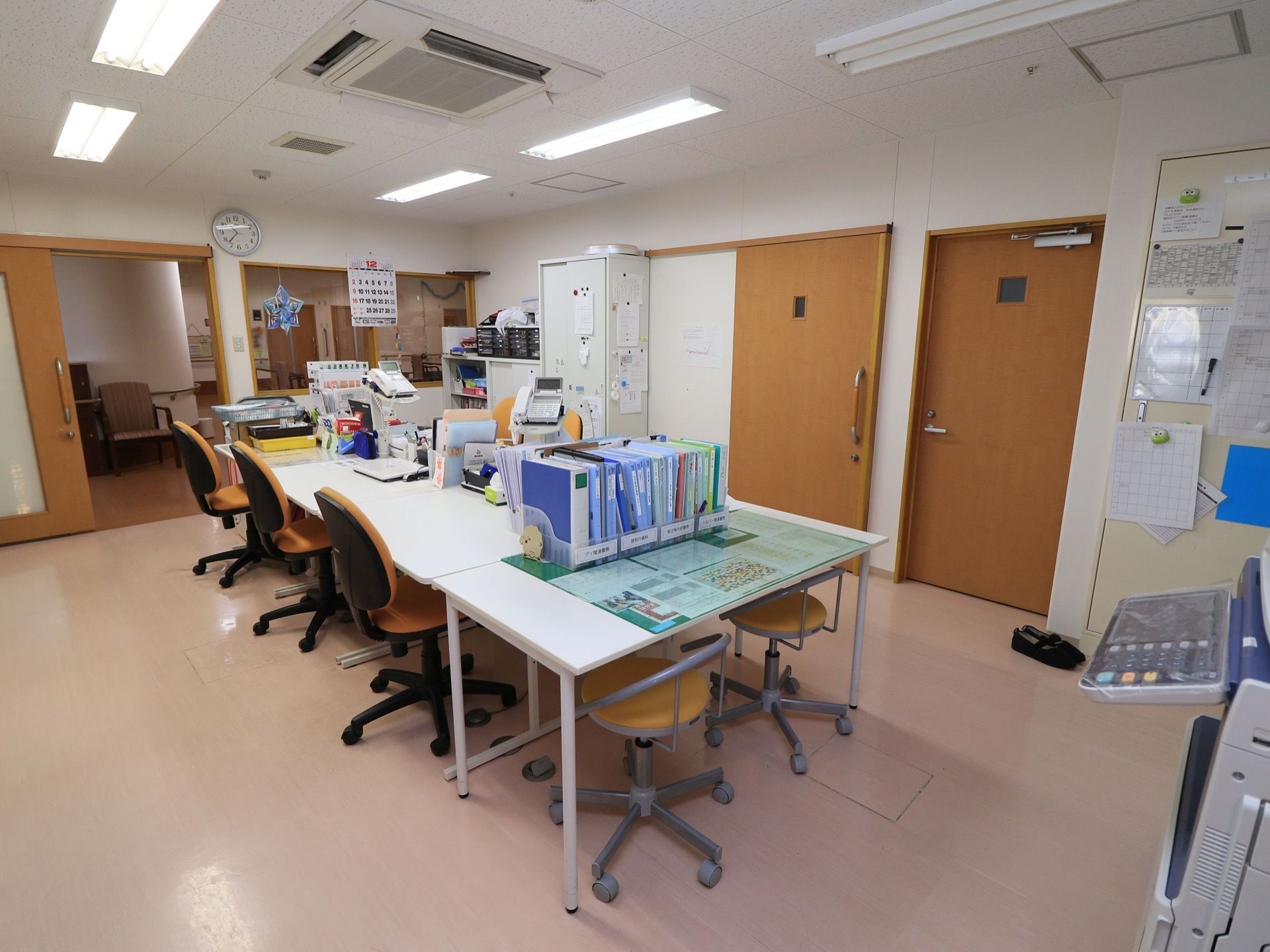 白いテーブルが向かい合わせに並べられ、それぞれキャスター付きの椅子が置いてある。一角には、さまざまなネームの貼ってあるファイルが置いてある。
