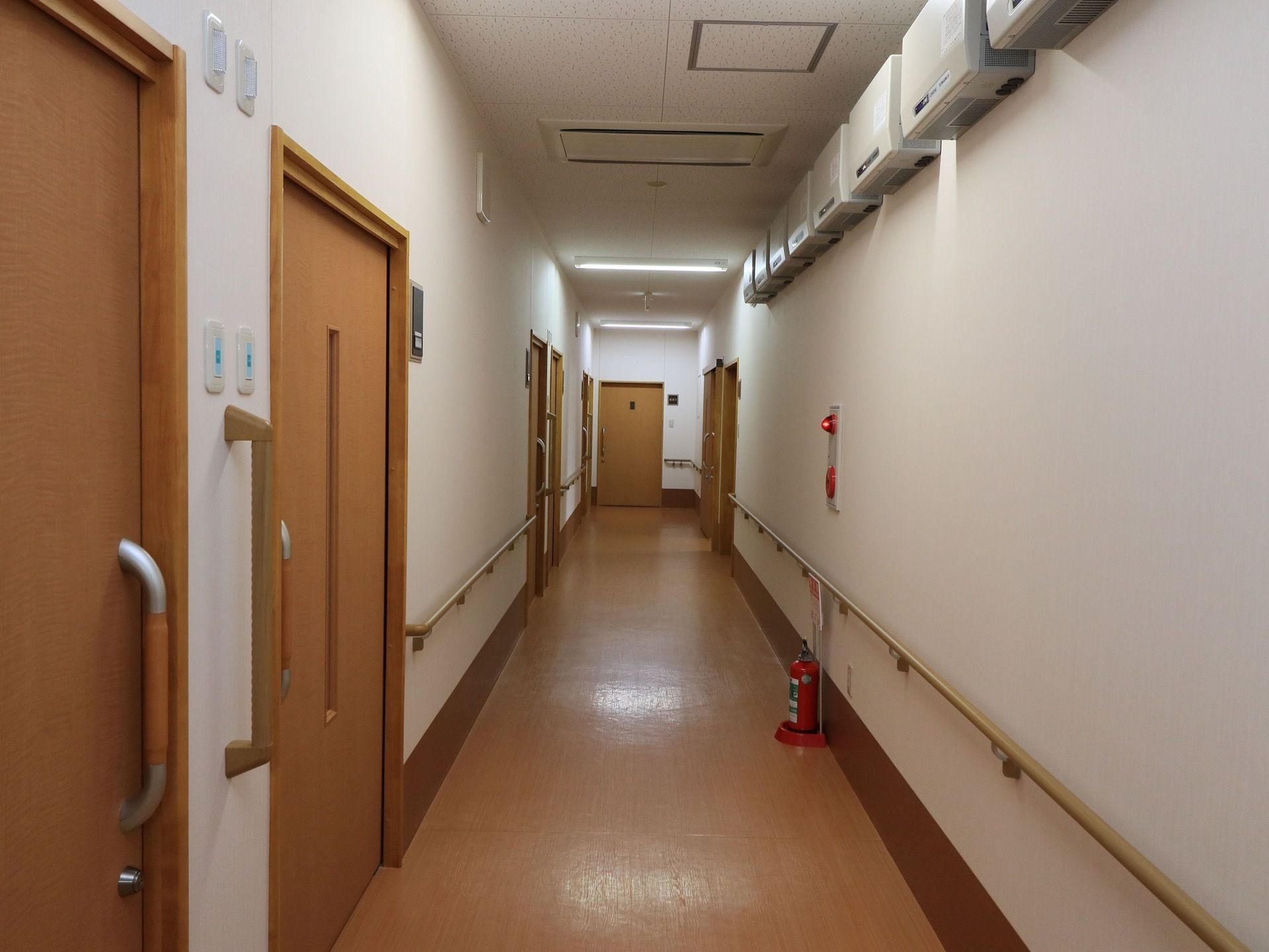廊下には、両側の壁に手すりが設置されている。壁には非常ベルがついている。その下に消火器も置かれている。