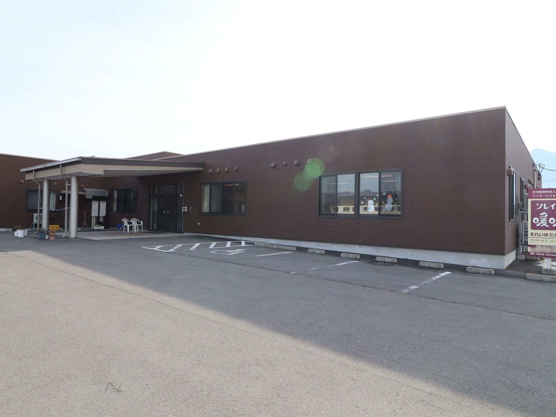 茶色を基調とした外壁の平屋建ての施設である。玄関前にはひさしが大きく張り出している。窓に季節の飾りつけがされている。