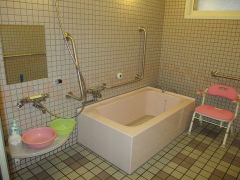 広々とした作りの浴室。ピンク色の浴槽はとても大きい。壁にはシャワーや手すりを取り付け、洗面器や椅子を用意している。