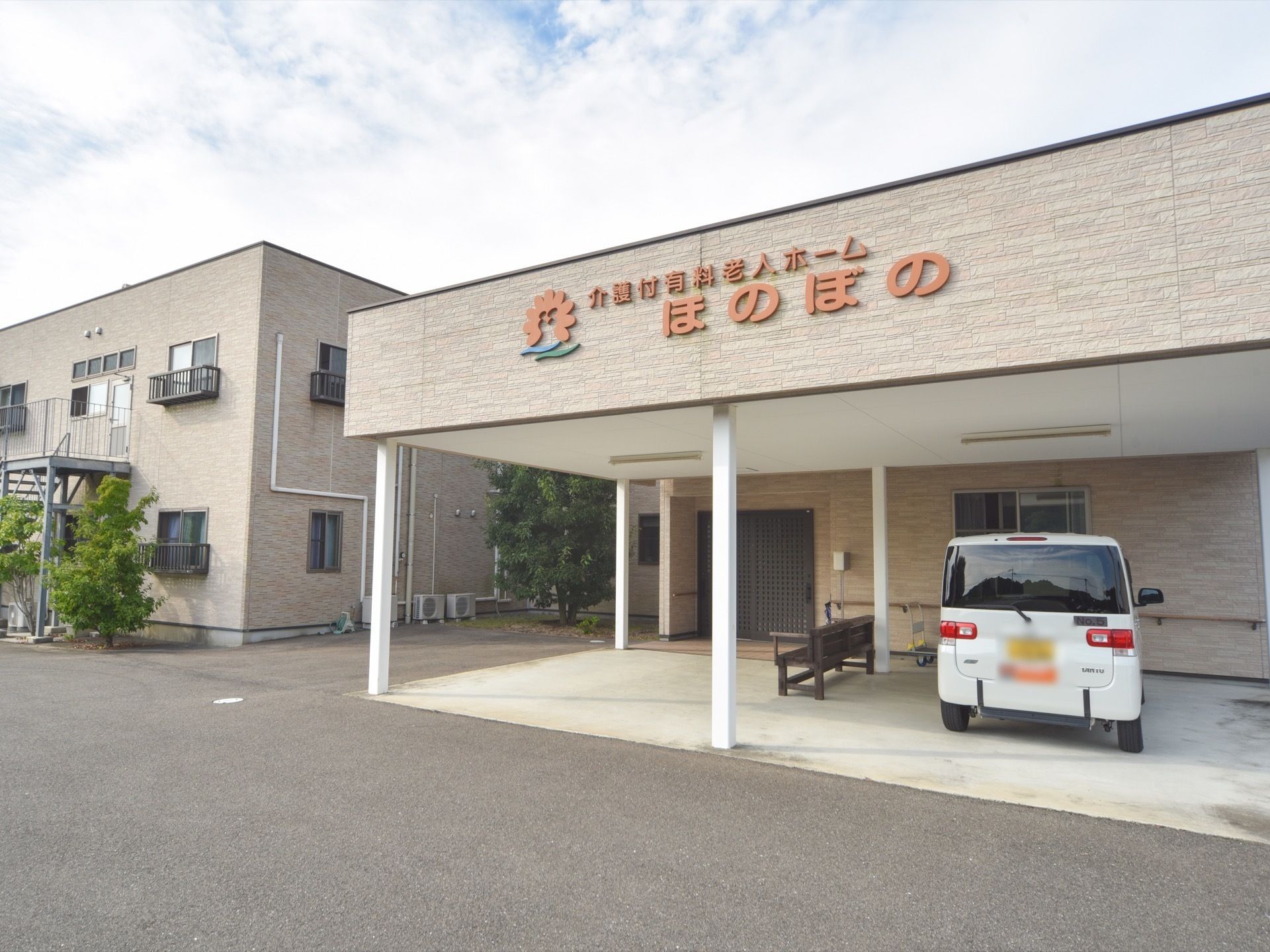 玄関のひさしの部分には、施設の名前とロゴが大きく表示されている。玄関の前のは、木のベンチが置かれている。