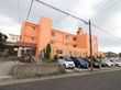 オレンジ色の外壁の施設で、スロープが玄関前に設置してある。建物を囲うかのように、植樹があちこちにしてある。