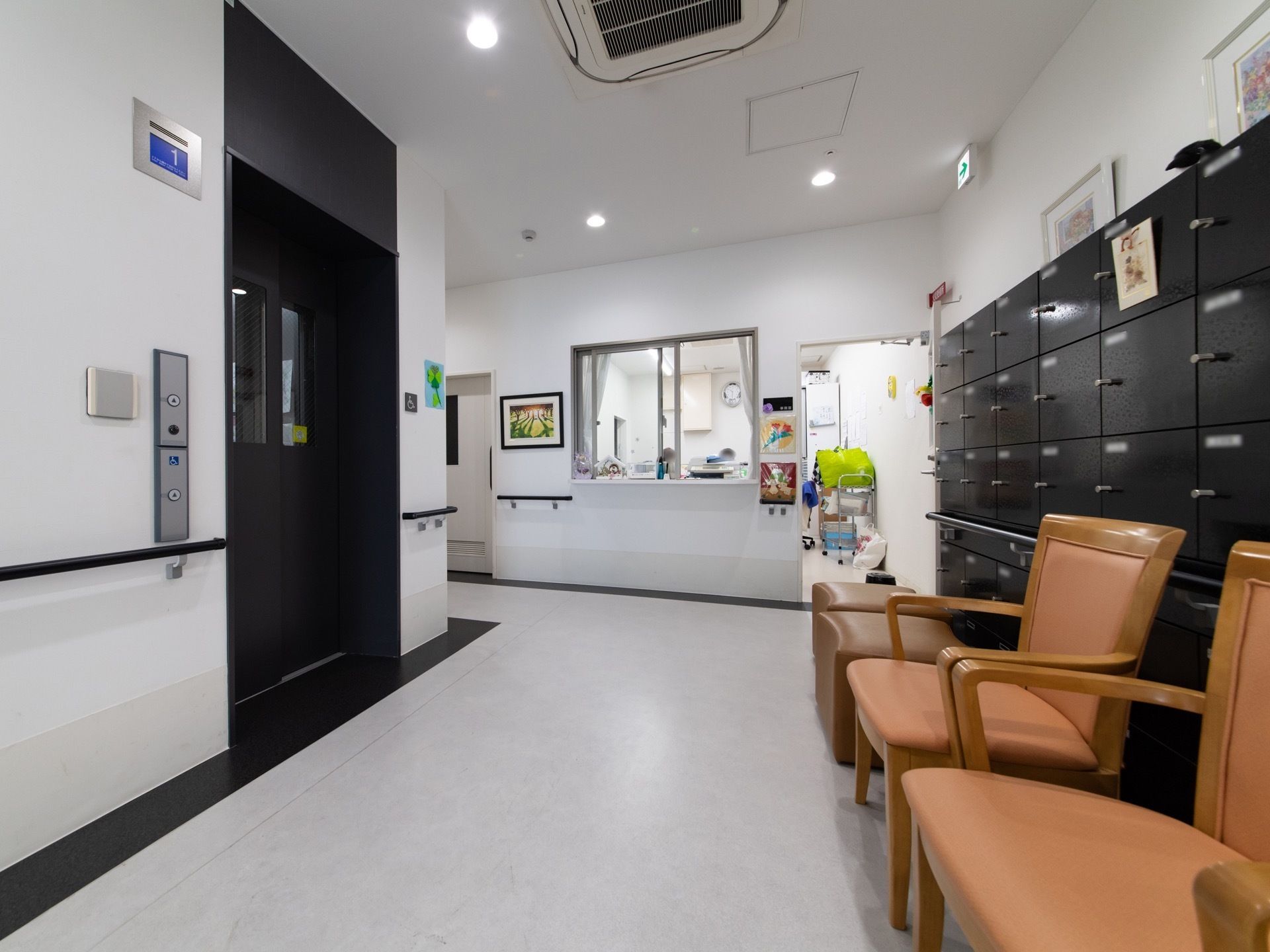 奥に小窓の設置された部屋がある。大きな下駄箱があり、その前に椅子が並んでいる。エレベーターが設置されている。