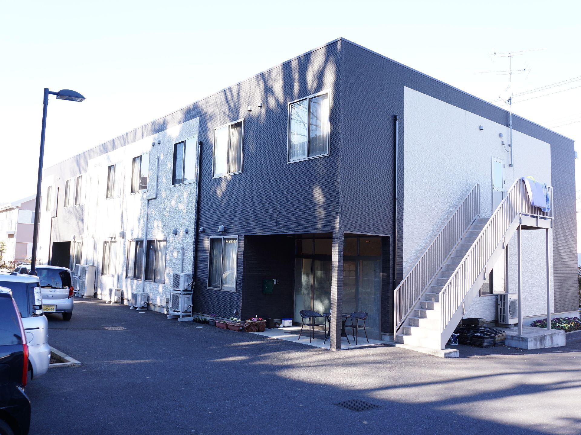 広々とした敷地に建つ2階建の施設は白と黒を基調としたスタイリッシュな外観。玄関前にはテーブルセットが配置され、憩いの場となっている。