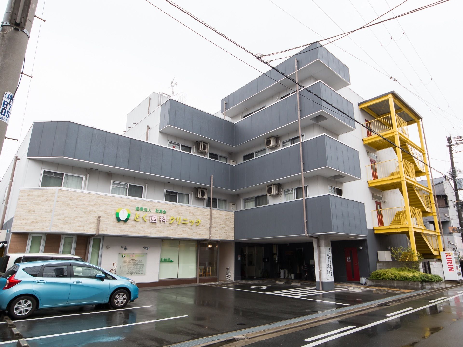 白い外壁にグレーのベランダが並んだ最大４階建ての建物である。施設の前は駐車場になっており、車が停まっている。