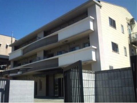 塀と門が備わっている敷地に建つ明るい色の三階建ての建物