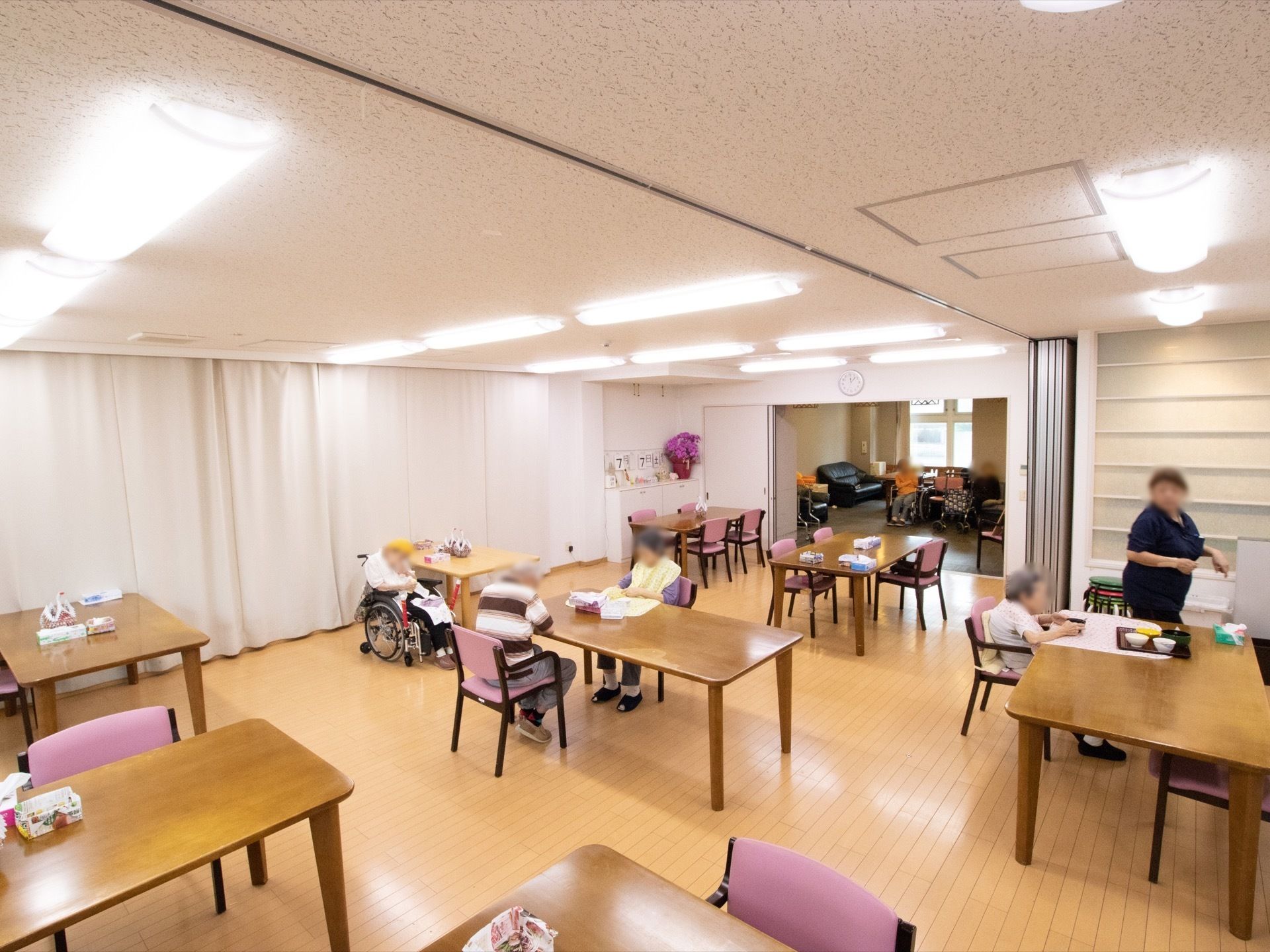 広々としたフローリングの食堂。収納型の壁で、必要に応じて２部屋に仕切ることができる。木製のテーブル、ピンクの椅子が並べられている。