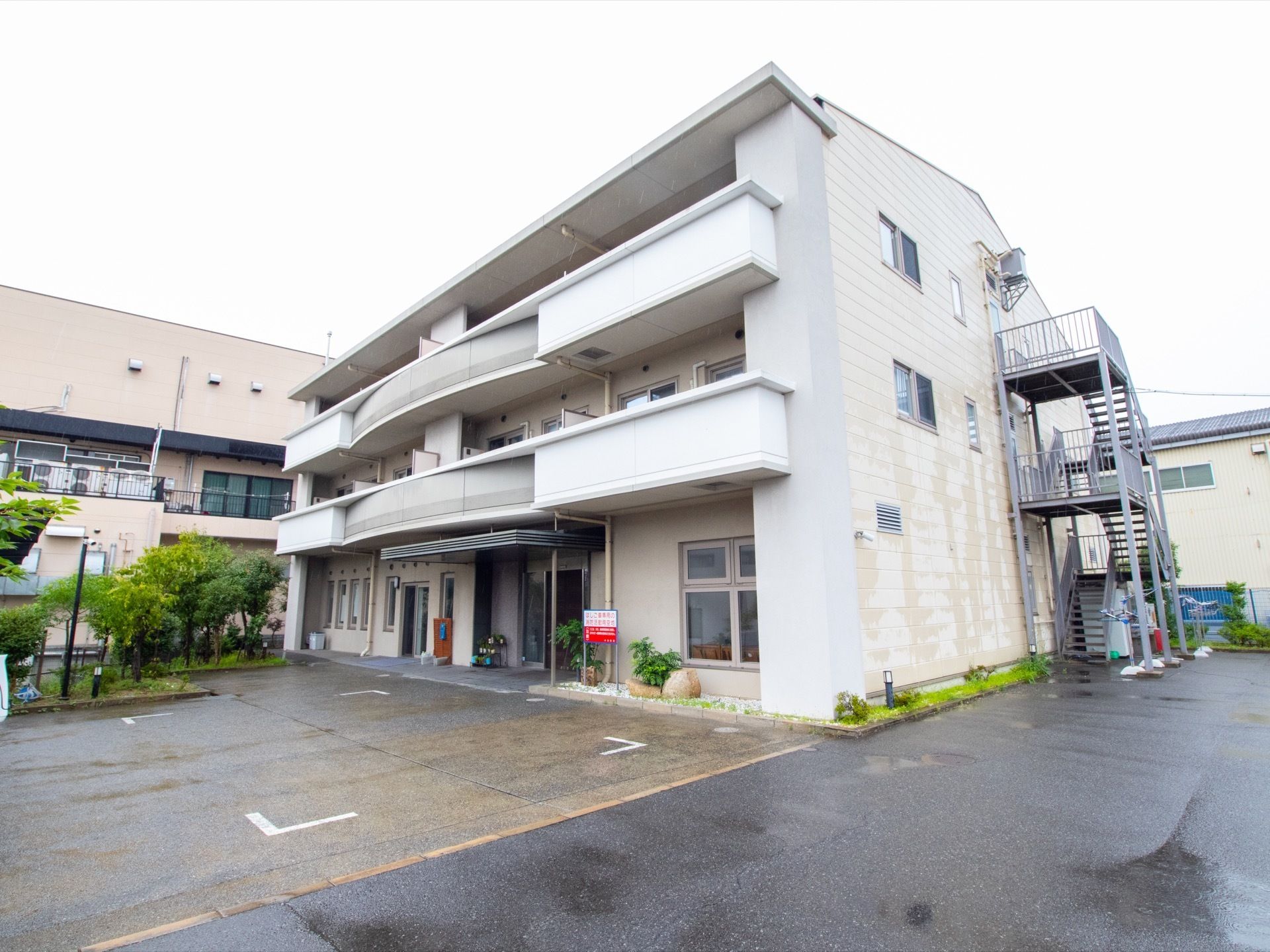 ３階建ての施設には幅の広い外階段がついている。建物の周囲には、花壇がめぐらされ、緑豊かな庭と駐車場が広がっている。