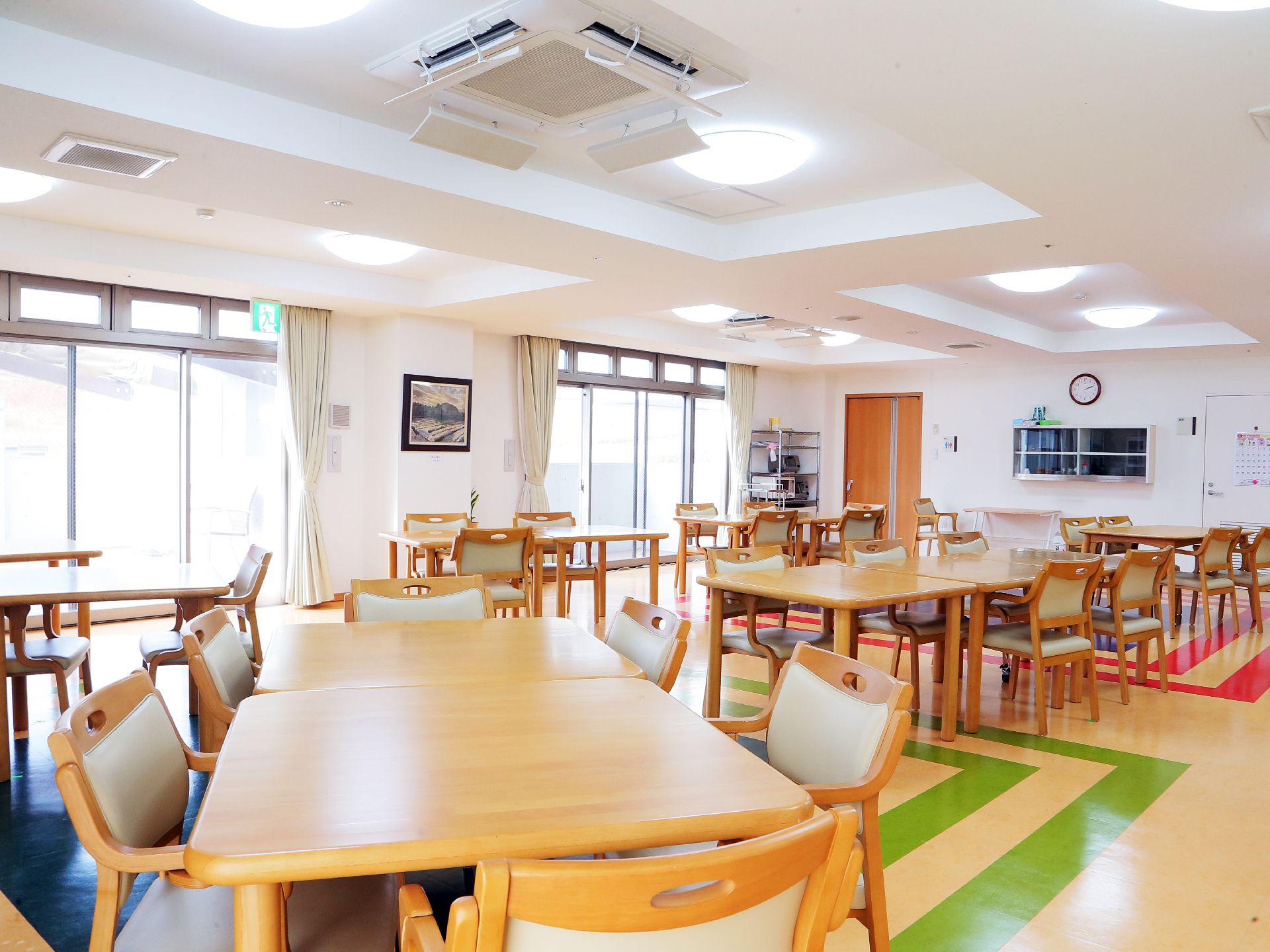 テーブルとイスが置かれた広々とした食堂。利用時間は７：３０・１２：００・１８：００。窓が大きく、明るい。