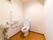白色基調のストライプの壁と明るめの茶系の床の内装のトイレである。壁にはエル型の手すりが設置され、小さな洗面台がある。