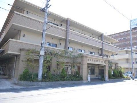 道路に面した側に植栽のある三階建てのどっしりとした建物