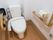 温水洗浄便座を備えた洋式トイレである。木目調の手すりが両側に設置されている。壁に白いペーパーホルダーがある。
