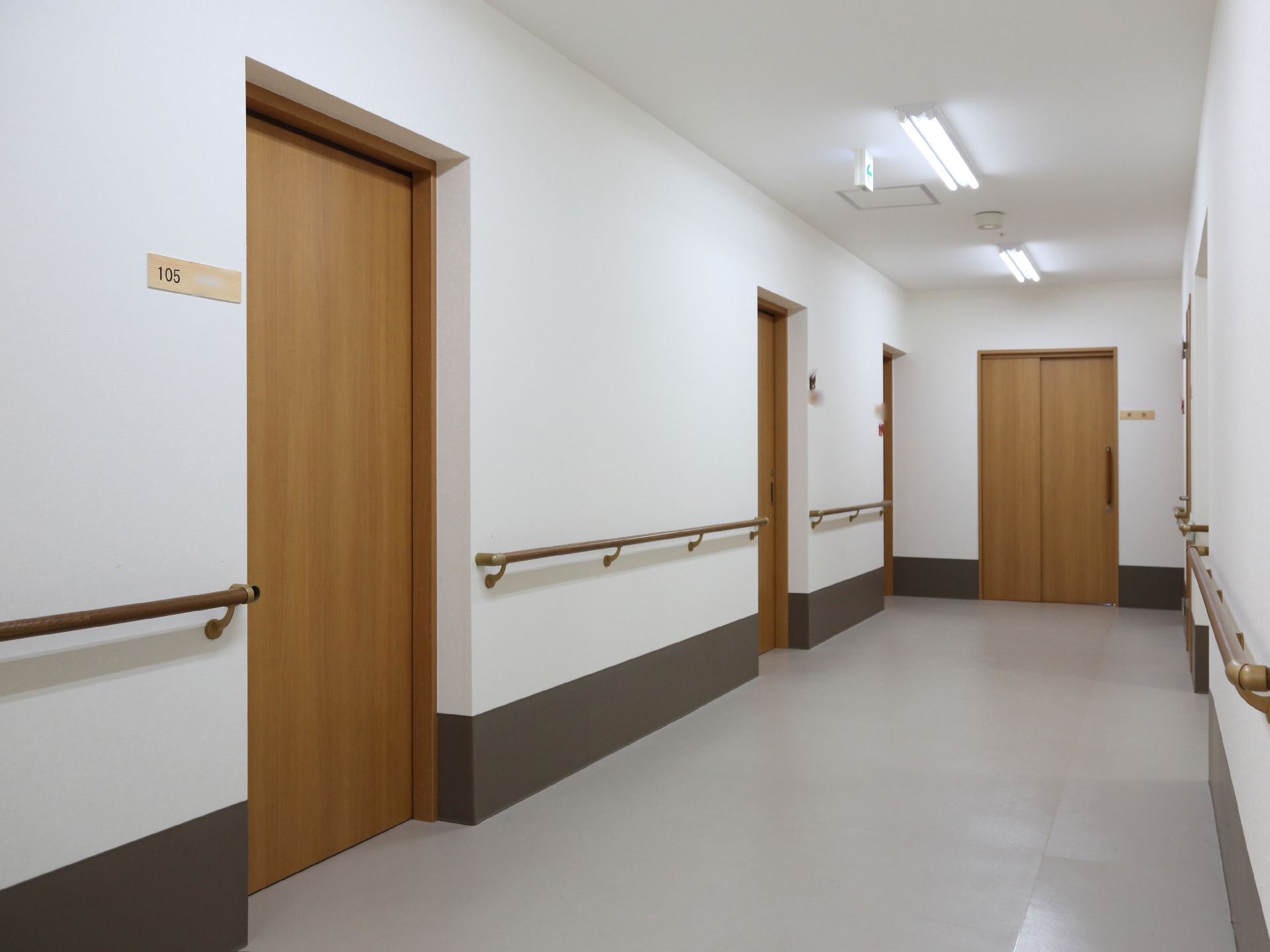 明るく広々とした通路。居室入り口横にも手すりが設置されている。居室のドアはスライド式で、十分な幅がある。