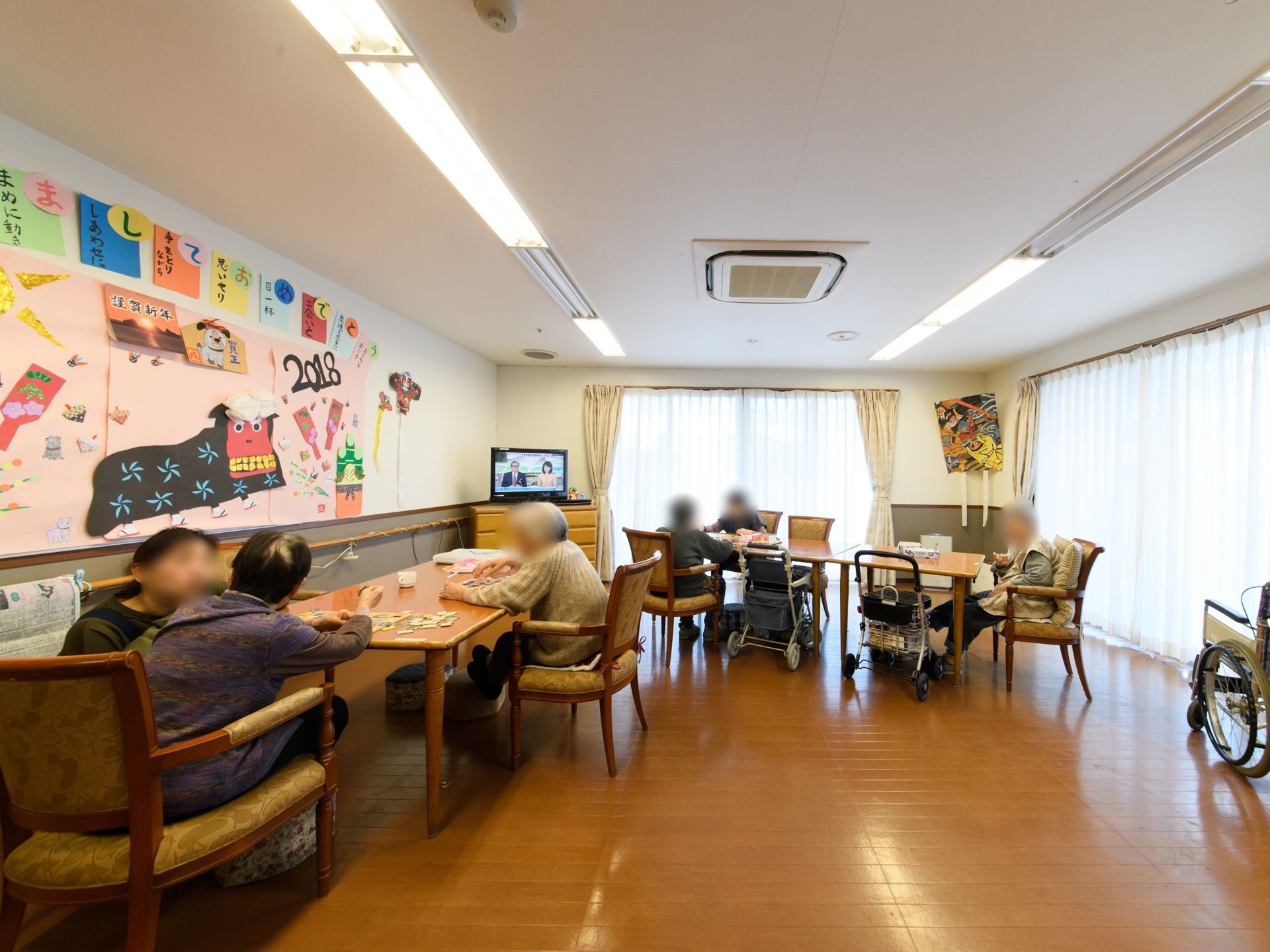 リビングにはテーブルと椅子、テレビが設置されている。壁にはあけましておめでとうの文字を使ってアクロスティックが作成されている。