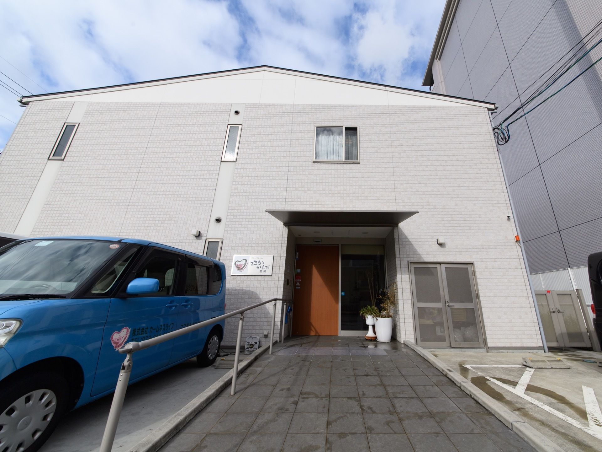 施設は薄いグレーのタイルが貼られている。入口には大きな屋根が取り付けられている。駐車スペースと入口を仕切るように手すりがある。