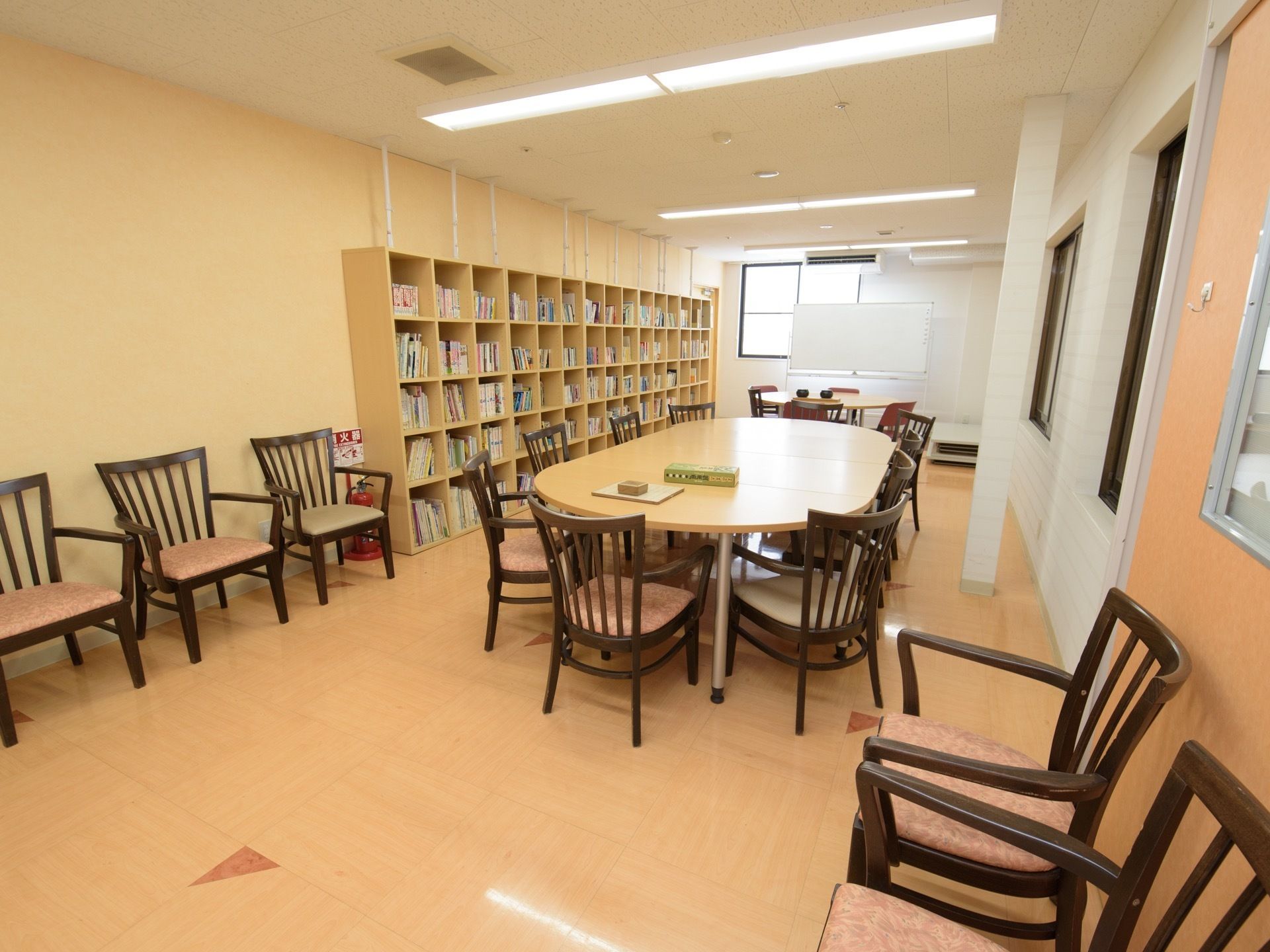 図書館の中央には楕円形の大きなテーブルが置かれており、まわりには椅子が並べられている。左の壁には本棚が設置されている。