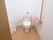 トイレの壁は白く、床はフローリングになっている。便座の両脇には手すりが設置されており、壁には呼び出しボタンなどが取り付けられている。