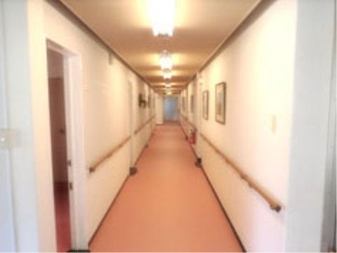 白色の壁に、両側には手摺があるバリアフリーの長い廊下