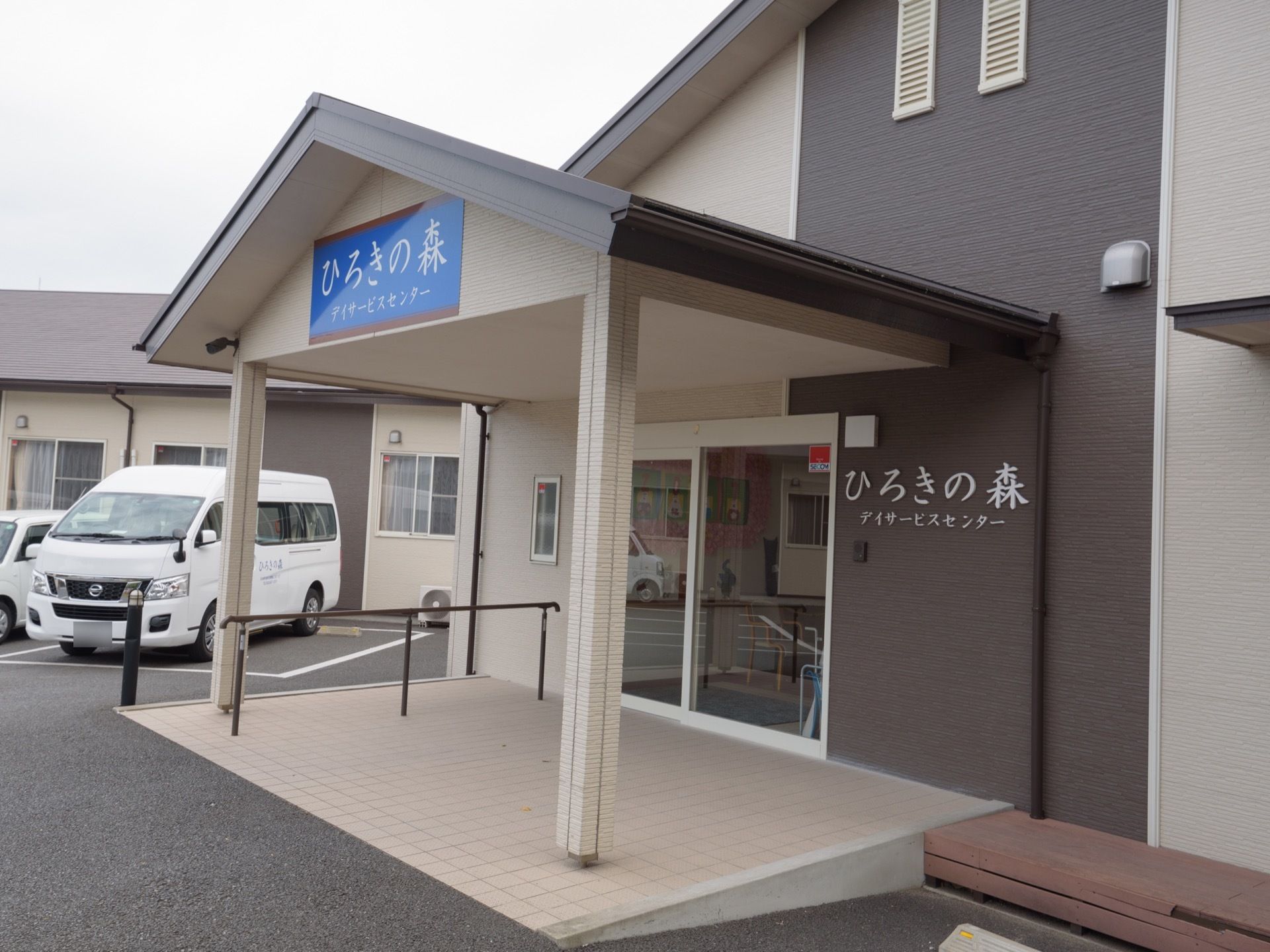 施設の玄関前の床はフラットなタイル敷きで、左側に手すりを取り付けている。上部には大きな三角の屋根を設置している。