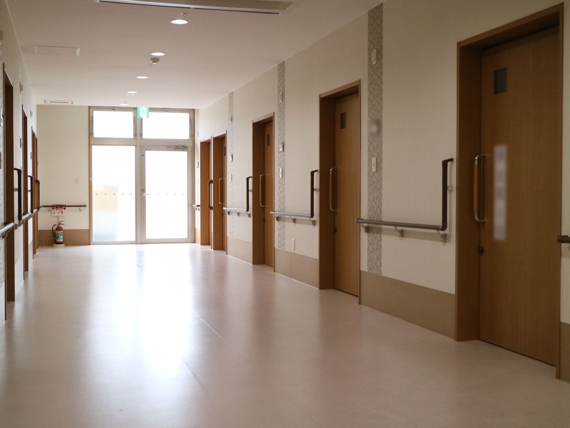 通路は広々としており、両側には部屋の扉が並んでいる。長い手すりが取りつけられている。通路の端には消火器が置かれている。