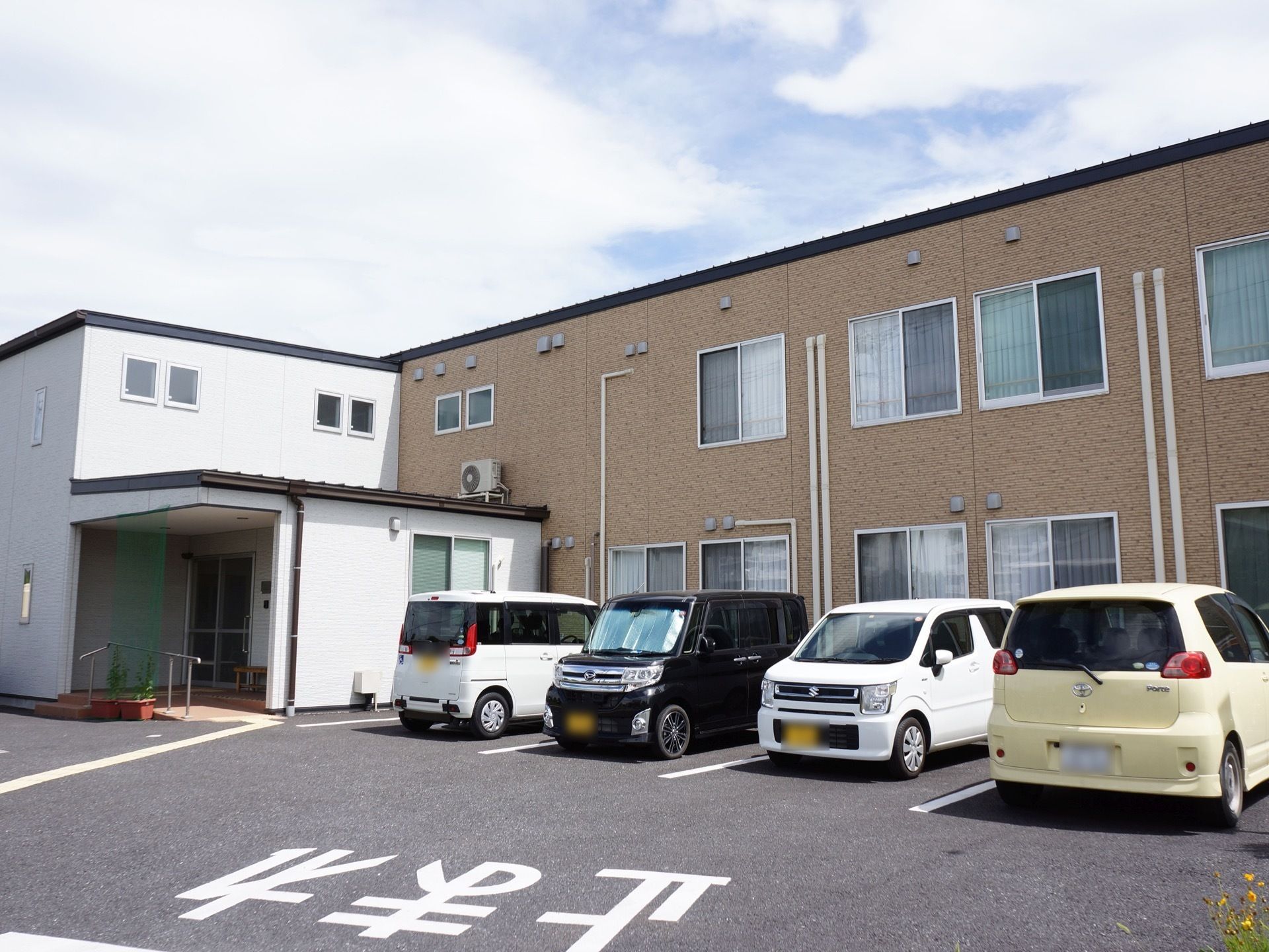 白と茶色の壁で構成された、２階建ての現代的な外観のホーム。左側に玄関があり、建物の前面には駐車場がある。