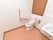 白色の壁に明るい茶系の床のトイレスペースである。便器上には、木目の両開きの収納棚がある。横には洗面台を設置している。