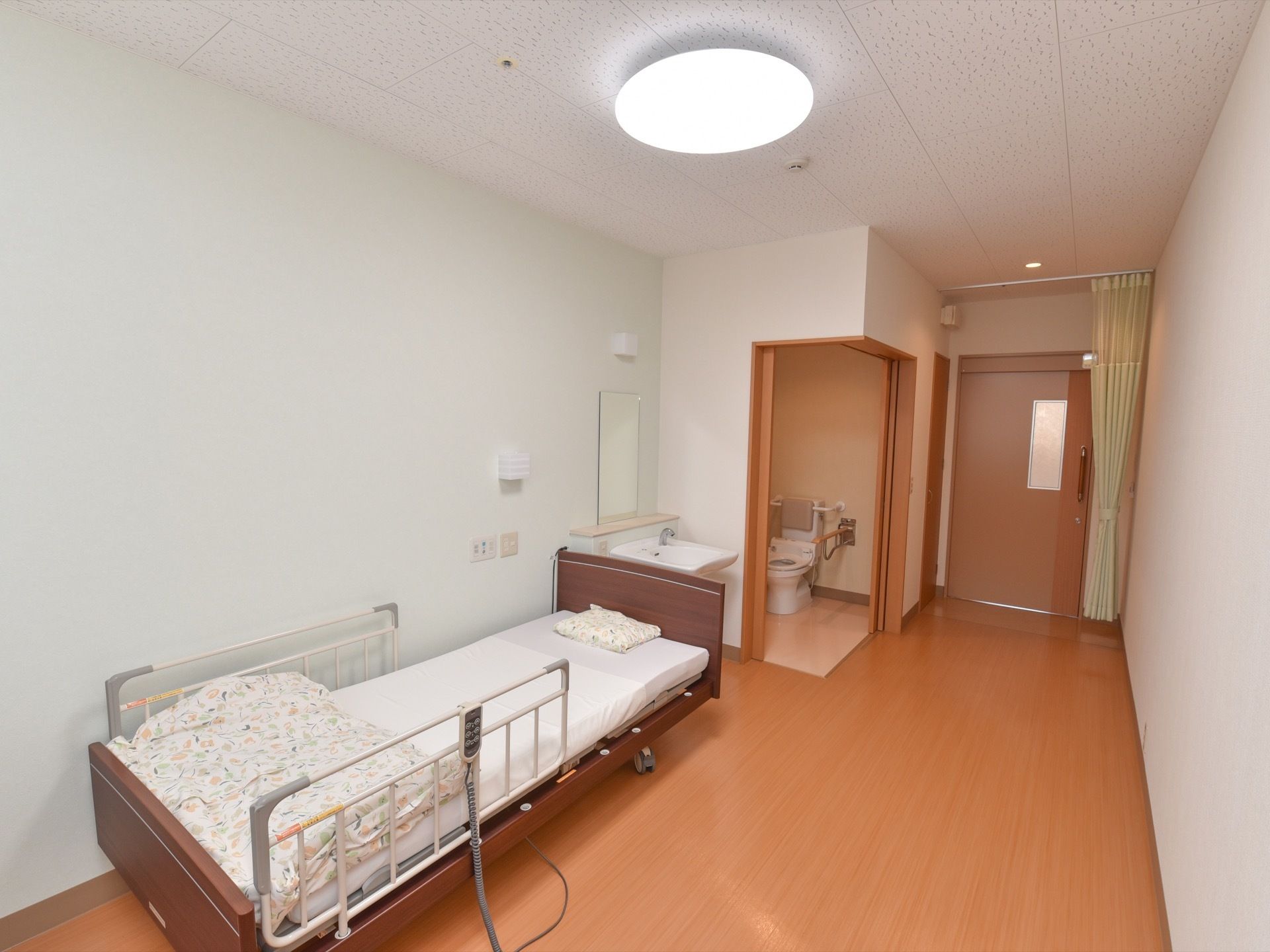 木目調の引き戸の出入口ドアから右側に直角にドアを開ける事ができるトイレスペースを設けている。出入り口ドア前にはカーテンを備えている。