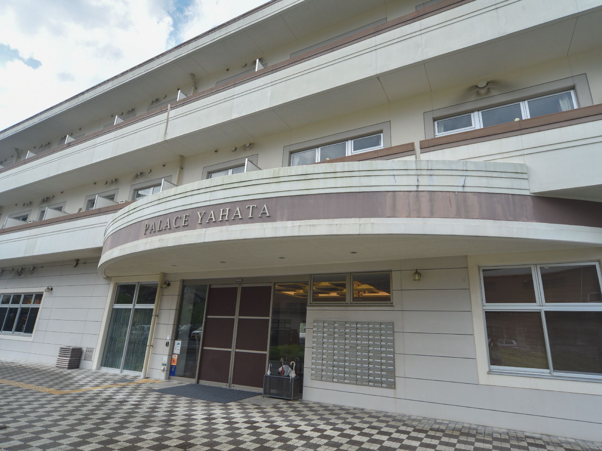 施設の玄関はダークブラウンの自動ドアで、両側はガラス張りになっている。上部の丸みを帯びた屋根には施設名が表示されている。