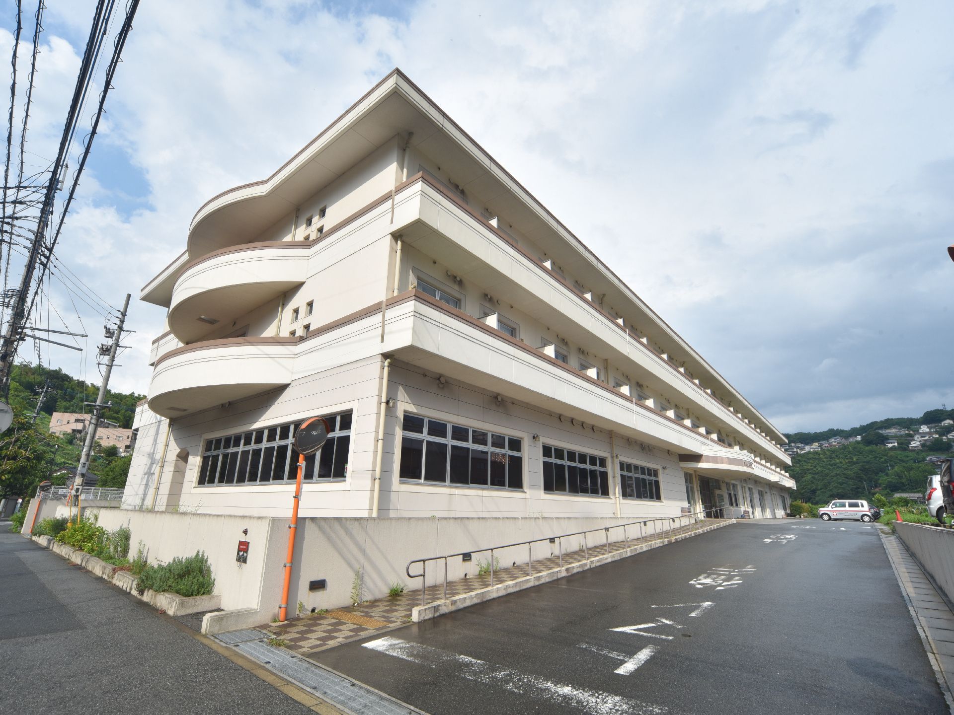 施設の建物の横には道路が通っており、入り口にはカーブミラーが設置されている。玄関へ向かってタイル敷きのスロープがある。