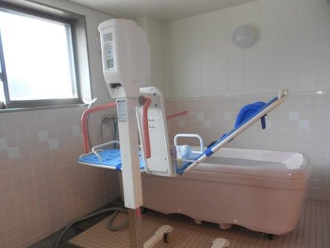 寝たままの姿勢で入浴できる介護用の浴槽が設置されている。窓から自然光の入る浴室はピンクの壁でやすらげる雰囲気である。